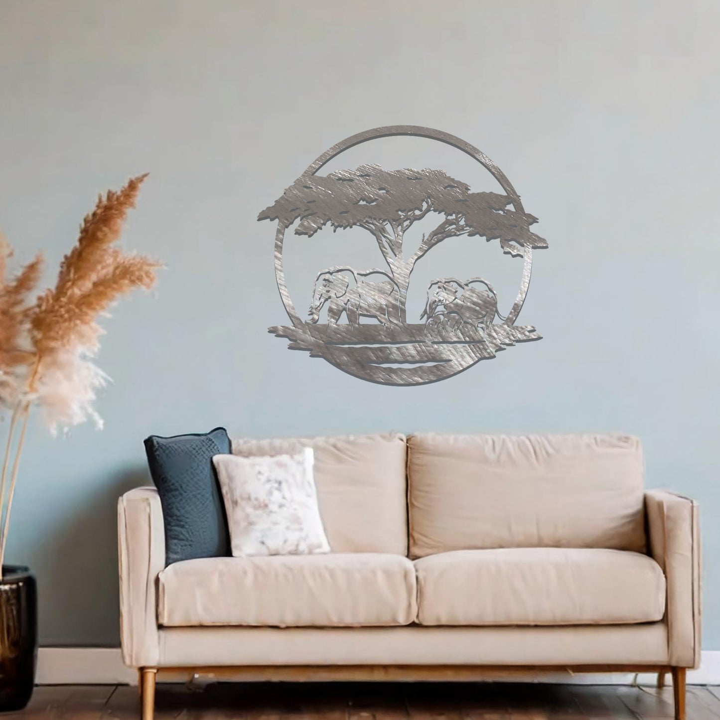 Metal wall art featuring a design of two elephants beneath a tree, framed in a circular shape. The art is placed on a neutral wall within modern room decor, creating a serene and nature-inspired atmosphere.