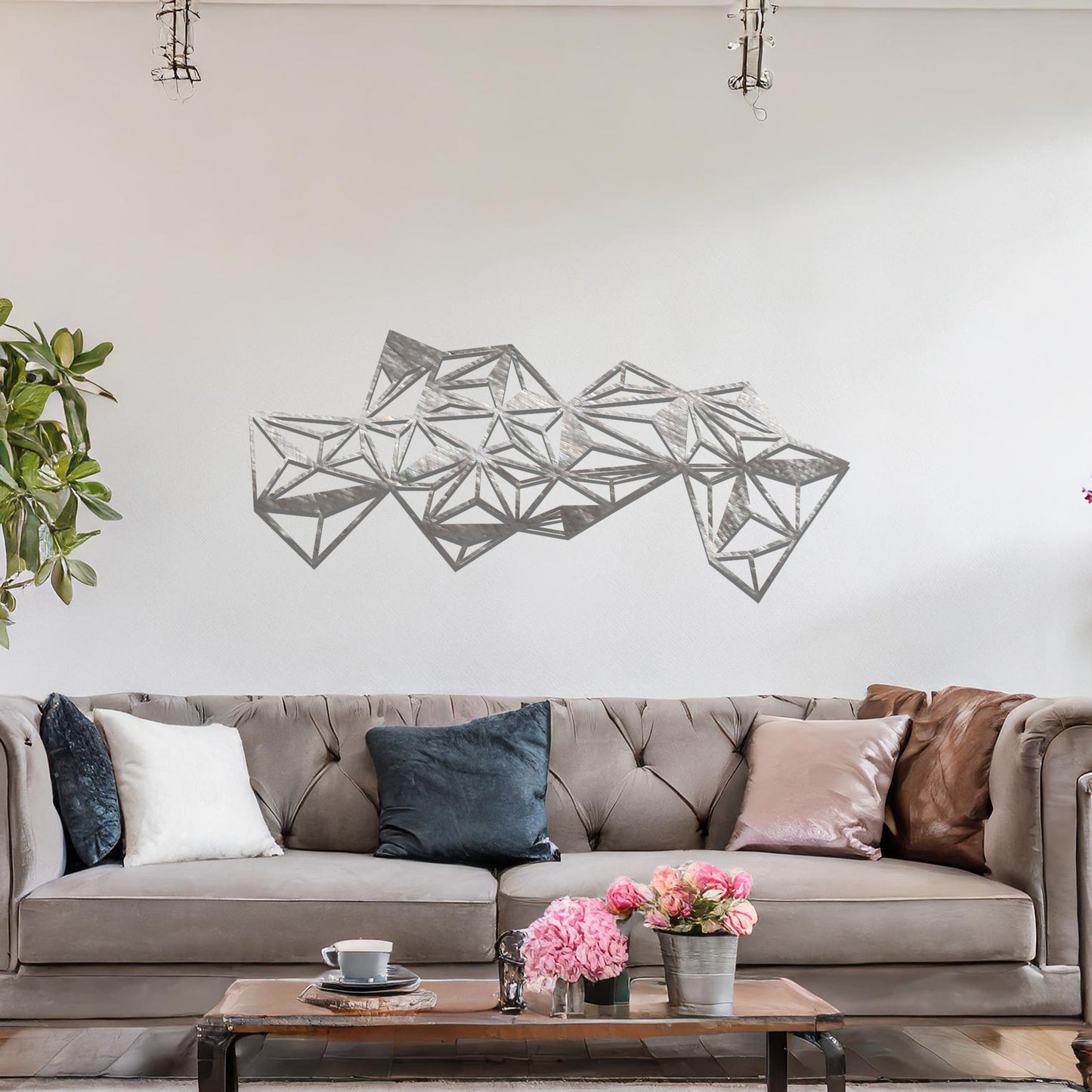 Metal wall art featuring an abstract geometric design with multiple interconnected triangular shapes, creating a dynamic, faceted pattern. The art is placed on a neutral wall within a modern room, complementing the vibrant decor with plants and furniture.