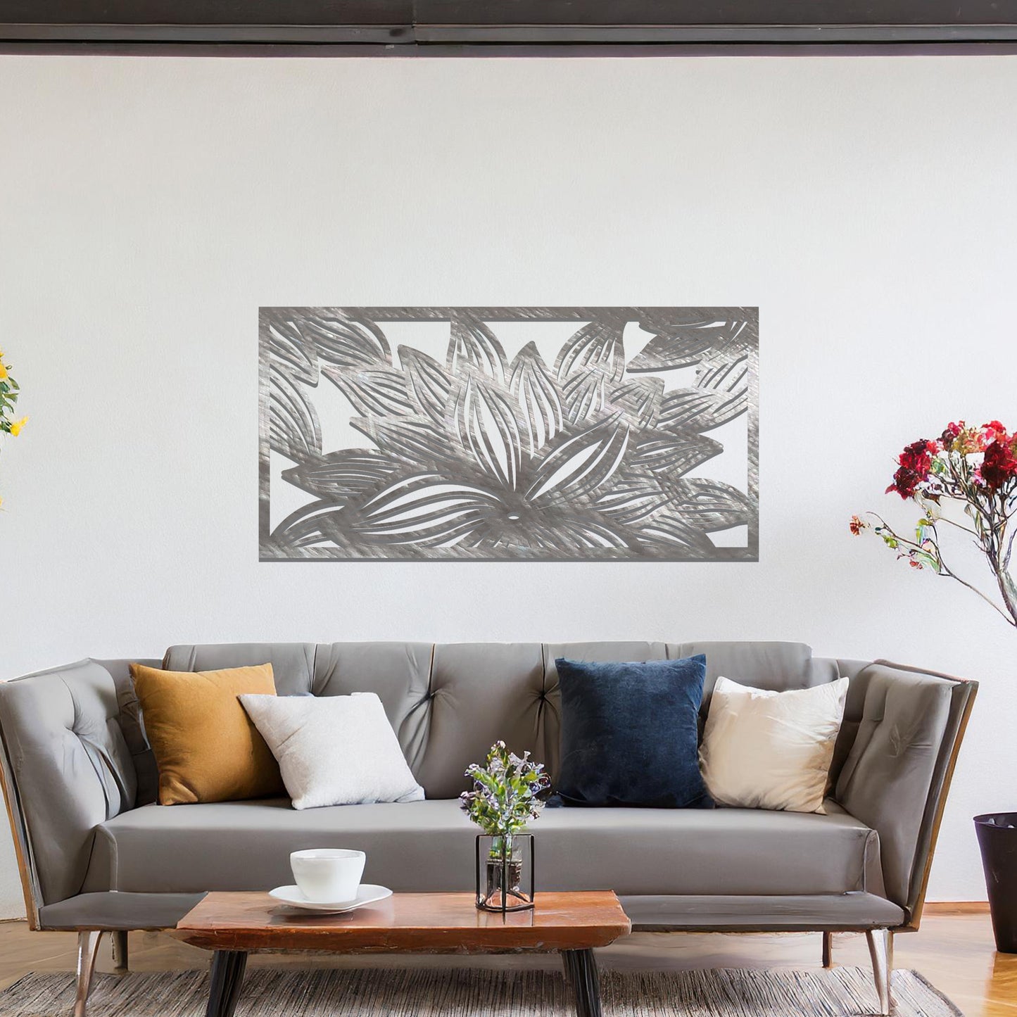 A metal wall art design showcasing a lotus flower with detailed, flowing petals. The design is framed within a rectangular shape. The art is displayed on a neutral wall within a modern living room setting, complementing the room's elegant decor.