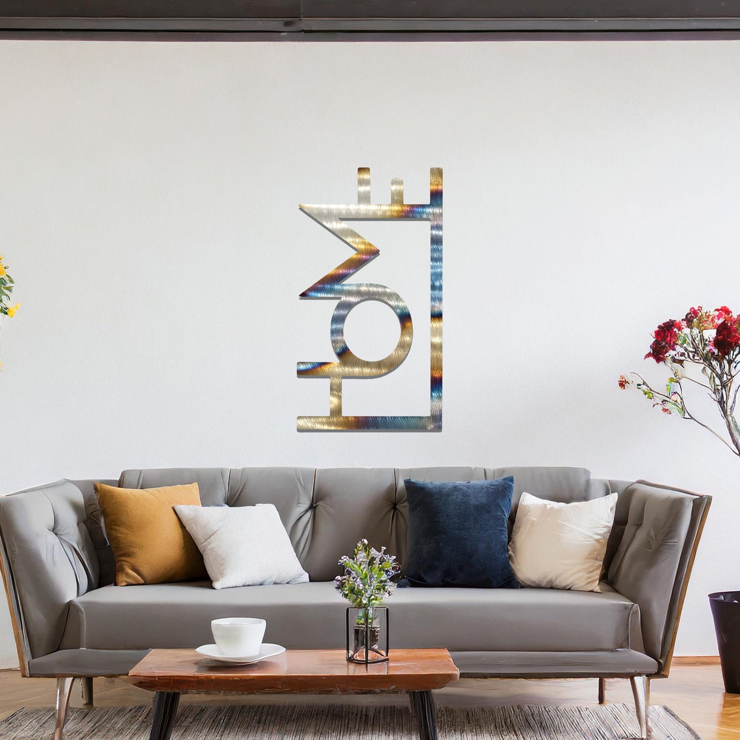 A modern metal wall art design featuring the word "HOME" in bold, geometric typography with an innovative, angular twist. The artwork is displayed on a neutral wall in a contemporary room setting.