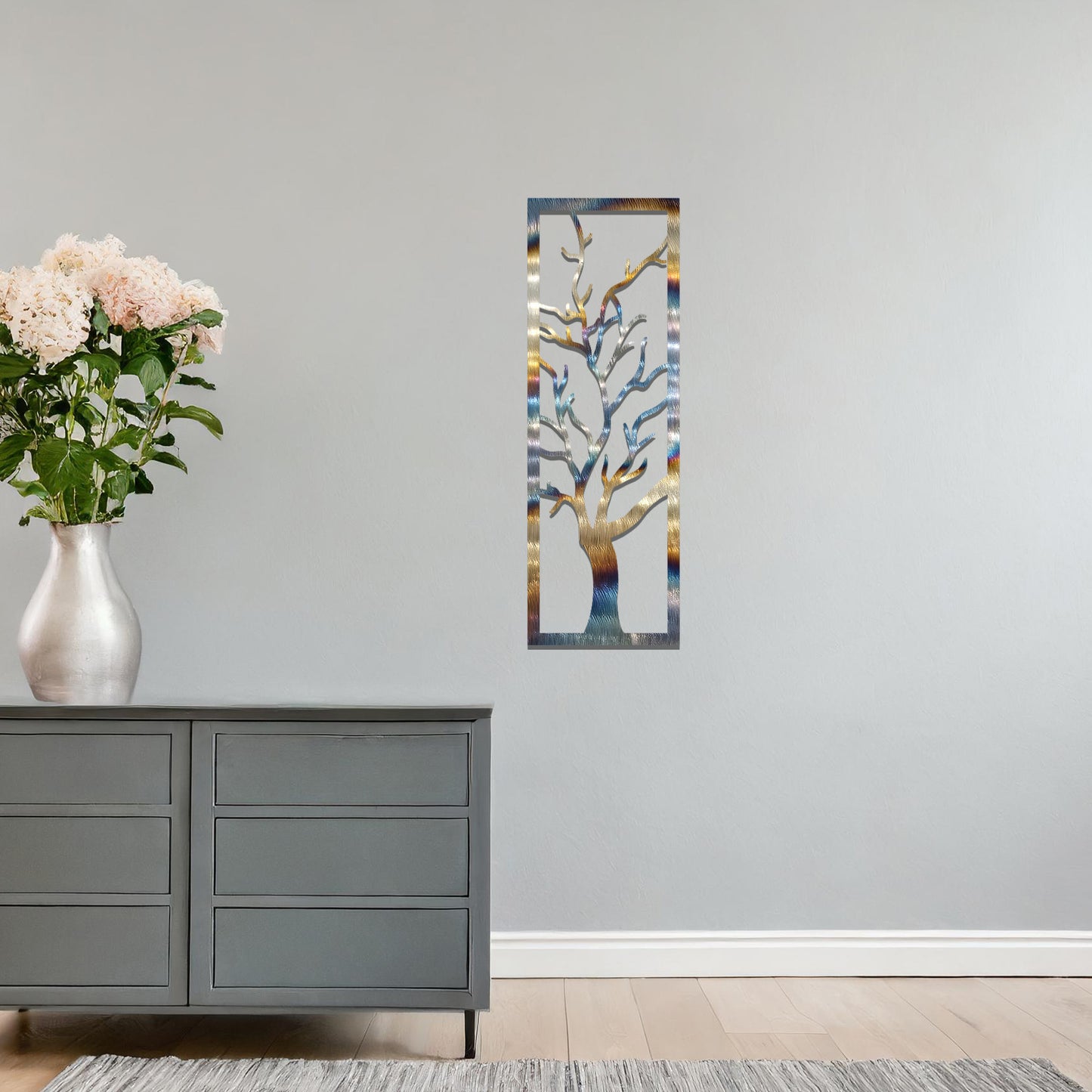 Metal wall art featuring a vertical design of a bare tree with intricate branches, mounted on a neutral wall within elegant room decor. The minimalist silhouette of the tree adds a sophisticated, natural focal point to the space.