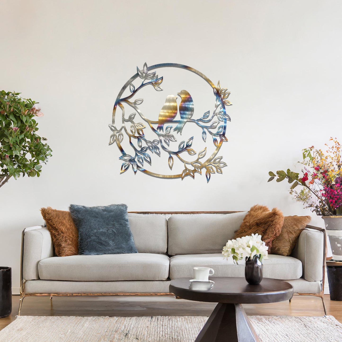 Metal wall art featuring a circular design with two birds perched on a branch surrounded by intricate leaves, adding a charming focal point to a beautifully styled living space.