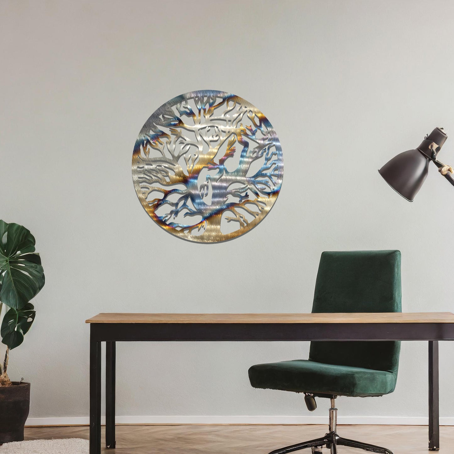 Metal wall art depicting a beautifully intricate tree design with twisting branches inside a circular frame. The artwork is placed on a neutral wall within a modern space, enhanced by the surrounding greenery and bookshelves.