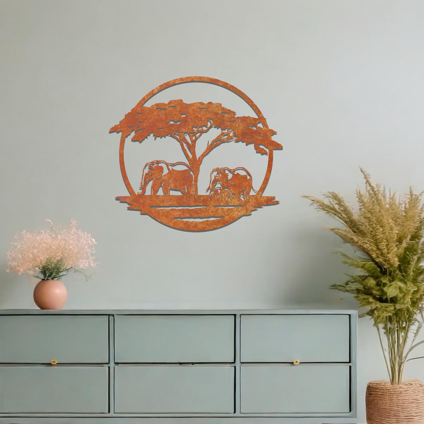 Metal wall art featuring a design of two elephants beneath a tree, framed in a circular shape. The art is placed on a neutral wall within modern room decor, creating a serene and nature-inspired atmosphere.