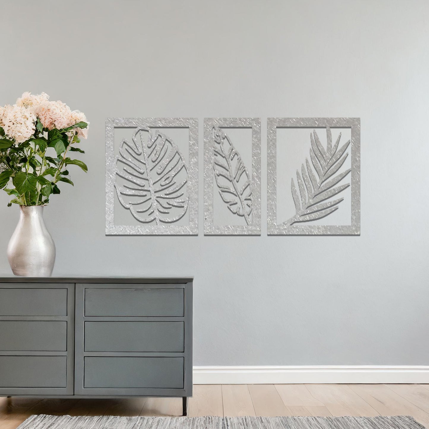 Metal wall art featuring a three-panel design with detailed leaf patterns, mounted on a neutral wall within modern decor. The organic motifs and rust finish create a natural, earthy focal point, enhancing the room's aesthetic.