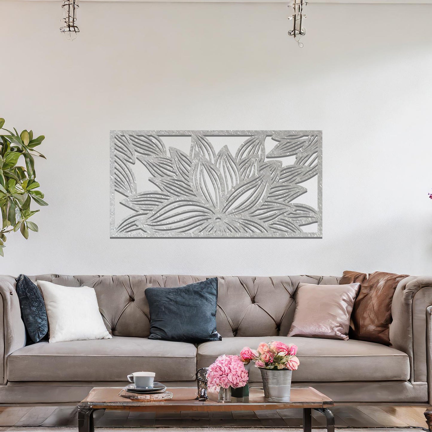 A metal wall art design showcasing a lotus flower with detailed, flowing petals. The design is framed within a rectangular shape. The art is displayed on a neutral wall within a modern living room setting, complementing the room's elegant decor.