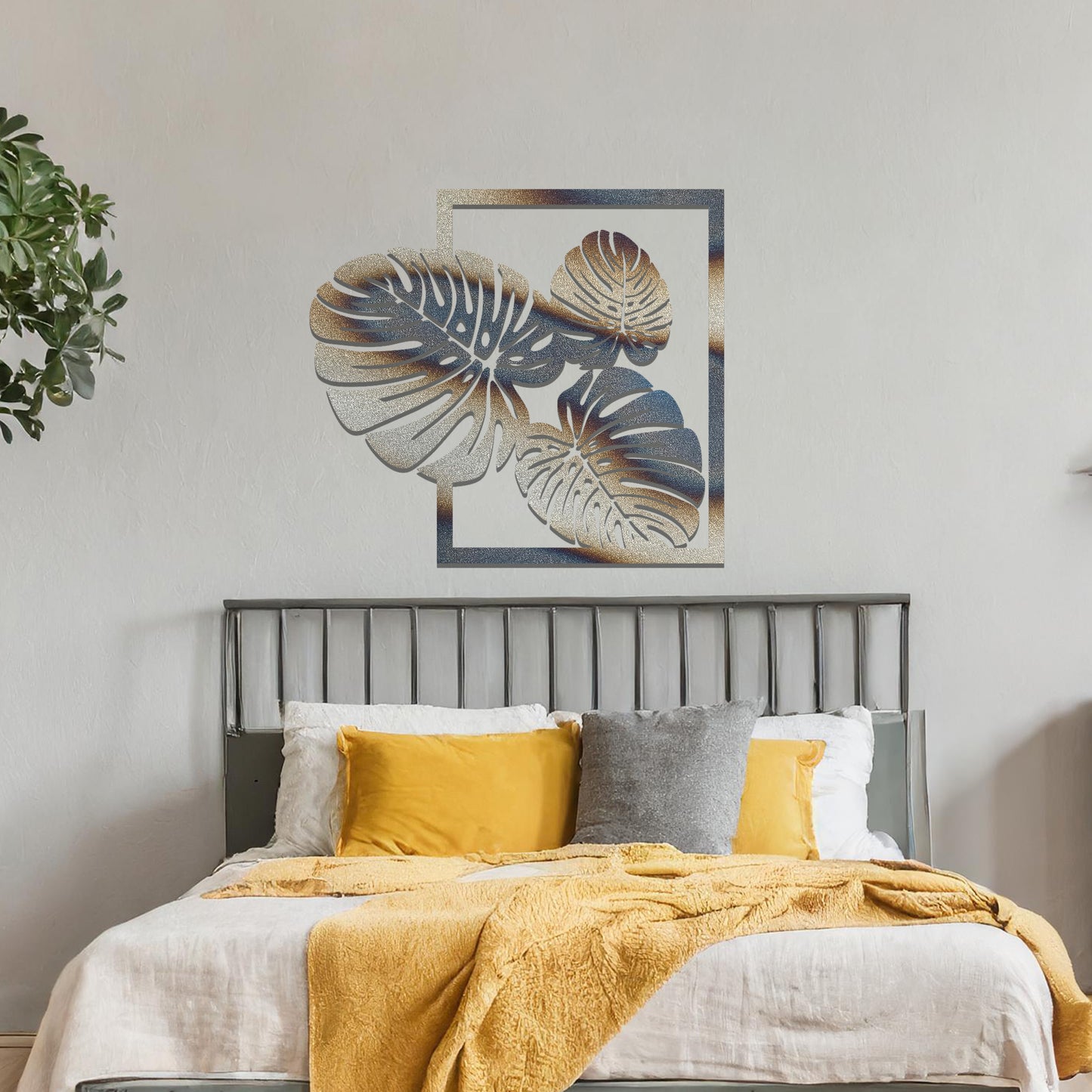Metal wall art featuring a design of three large, detailed Monstera leaves arranged within a rectangular frame. The intricate cut-out pattern highlights the natural lines and veins of the leaves. The artwork is displayed against a neutral wall in a modern setting.
