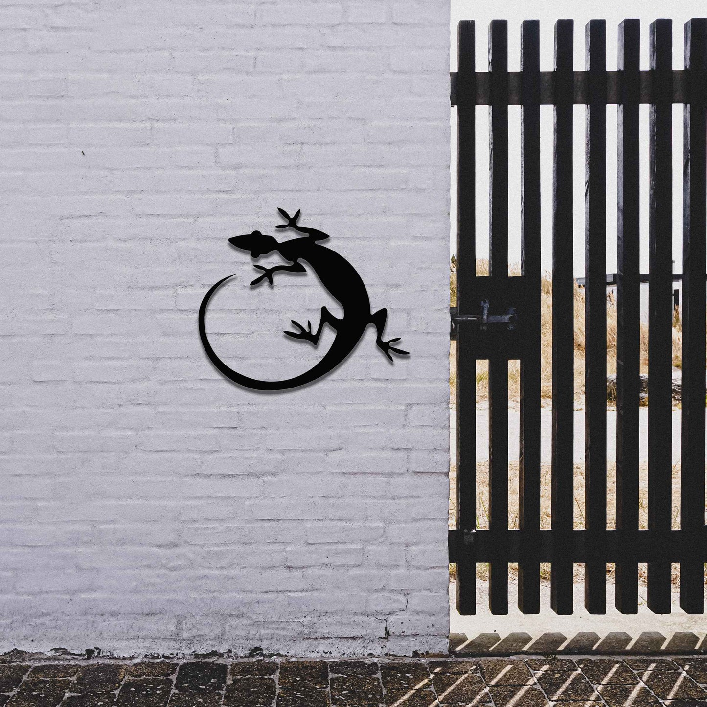 Metal garden decoration featuring a gecko silhouette design with a curved tail, adding a sleek and contemporary accent to outdoor walls, seamlessly complementing rustic and minimalist spaces.