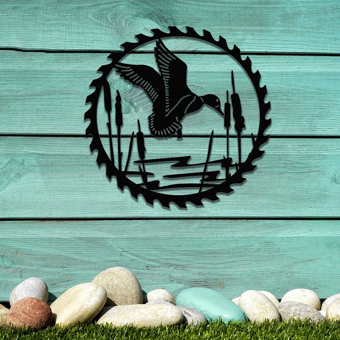 Metal garden decoration featuring a duck in flight over a pond surrounded by cattails, enclosed within a circular saw blade design, combining rustic charm and outdoor-inspired artistry to enhance garden or wall decor.