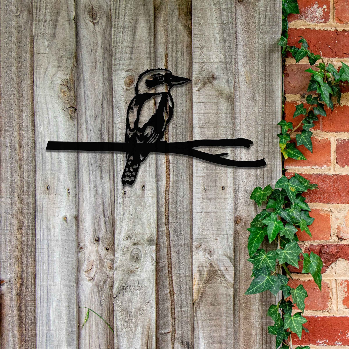 Metal garden decoration featuring a kingfisher perched on a branch with intricate cutout details and a rustic finish, designed to enhance walls or fences, adding a natural and elegant touch to outdoor spaces.