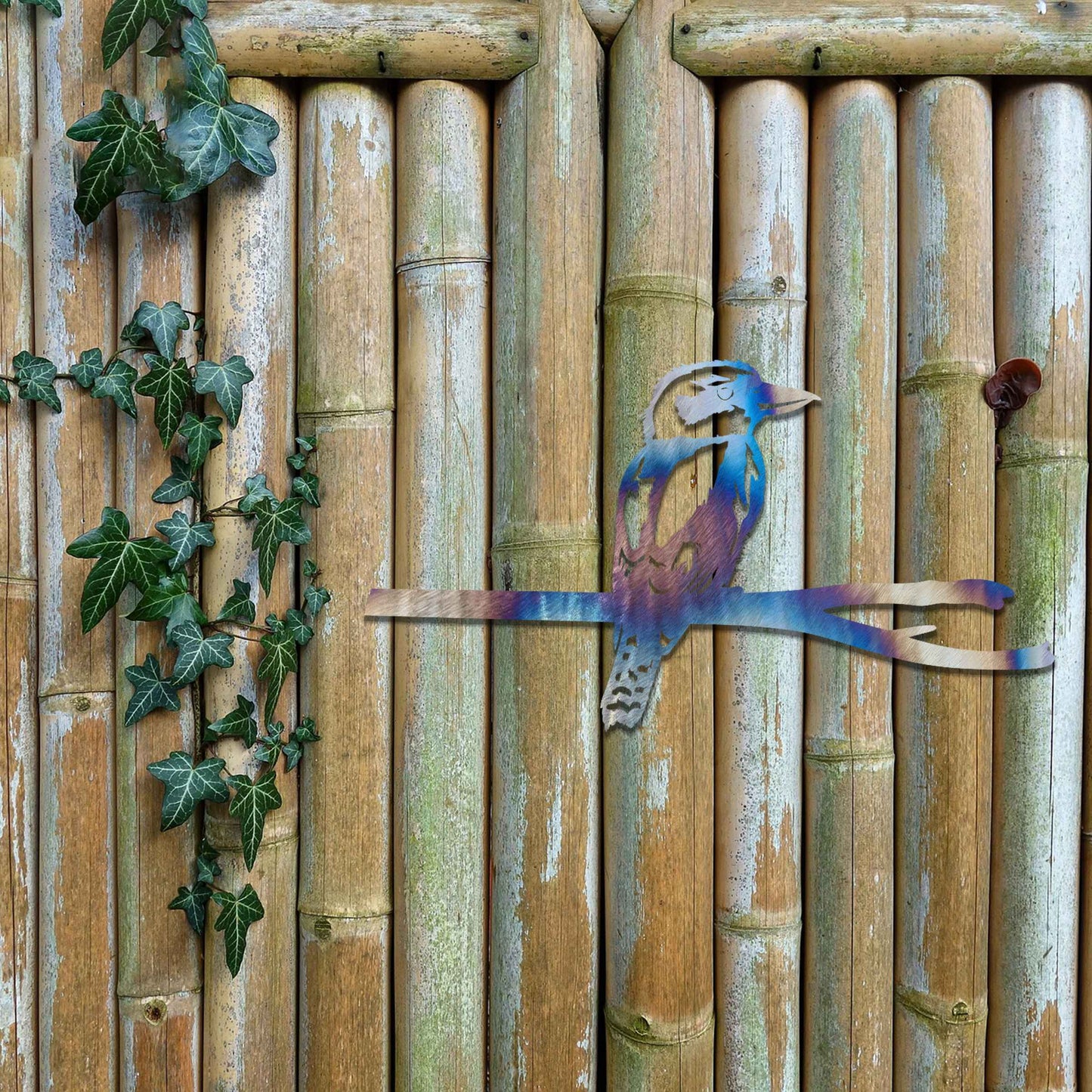 Metal garden decoration featuring a kingfisher perched on a branch with intricate cutout details and a rustic finish, designed to enhance walls or fences, adding a natural and elegant touch to outdoor spaces.