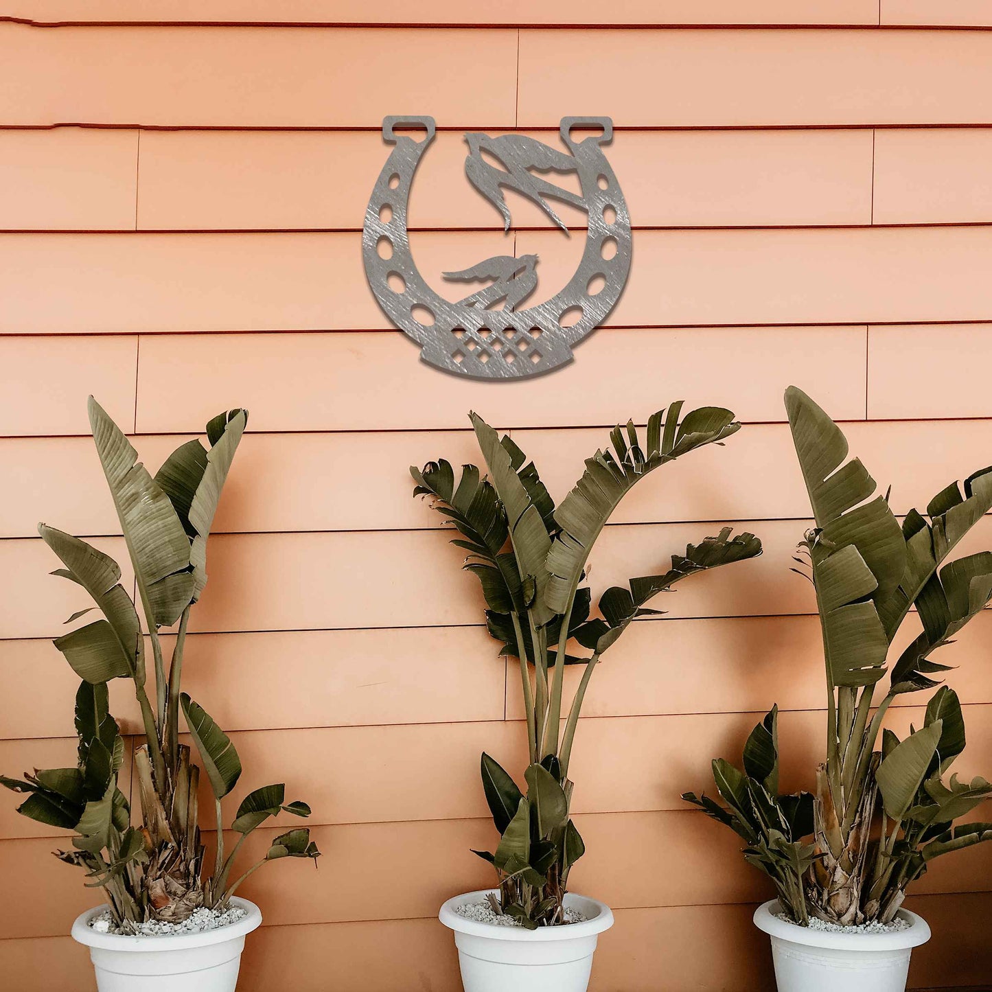 Metal garden decoration featuring two swallows perched within a horseshoe design, crafted with intricate detailing to symbolise luck and harmony, adding a rustic and charming touch to outdoor walls or fences.