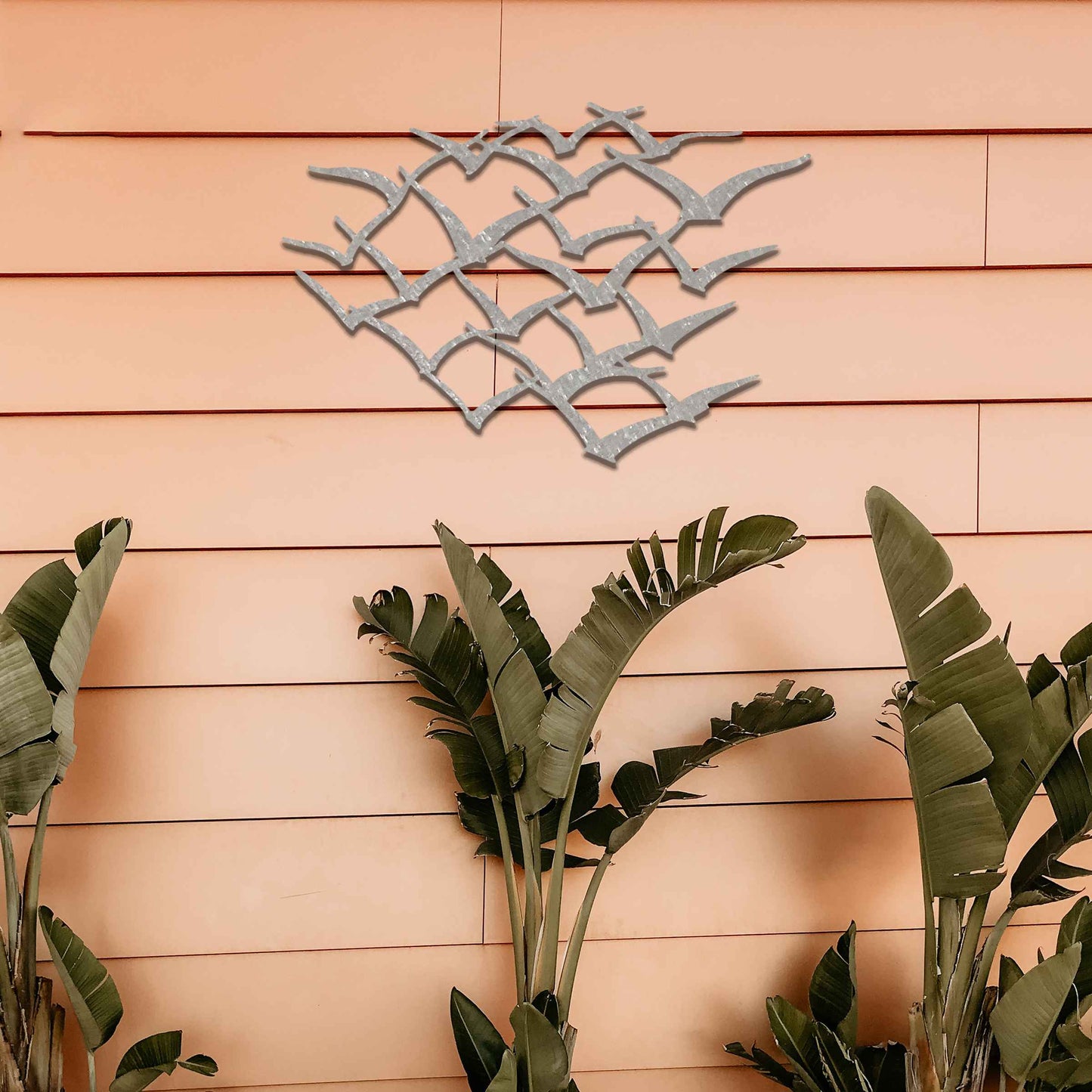 A stunning metal wall art featuring an abstract flock of birds in flight. This dynamic piece brings an element of freedom and movement to your space, complementing lush green surroundings for a serene and modern aesthetic.