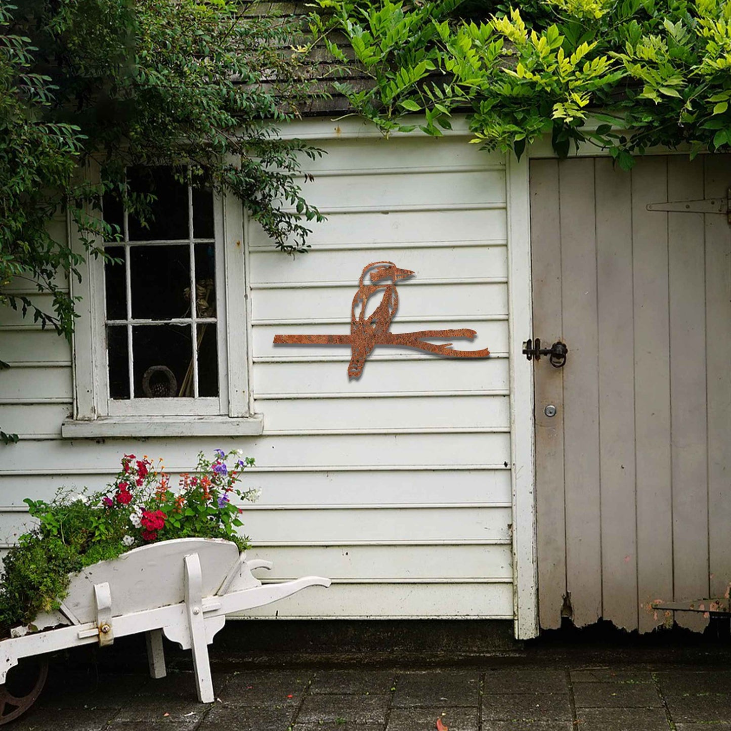 Metal garden decoration featuring a kingfisher perched on a branch with intricate cutout details and a rustic finish, designed to enhance walls or fences, adding a natural and elegant touch to outdoor spaces.