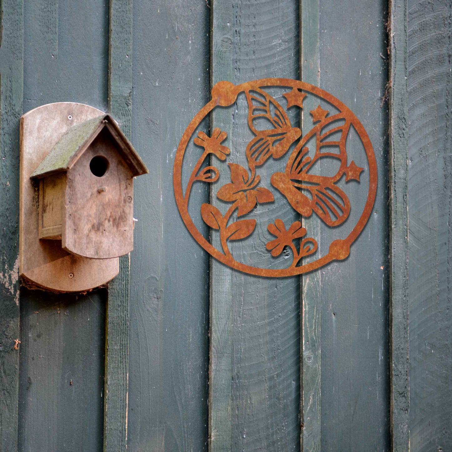 Metal garden decoration featuring a circular design with butterflies, flowers, and stars, crafted with a rustic finish, adding a whimsical and nature-inspired charm to outdoor walls or fences.