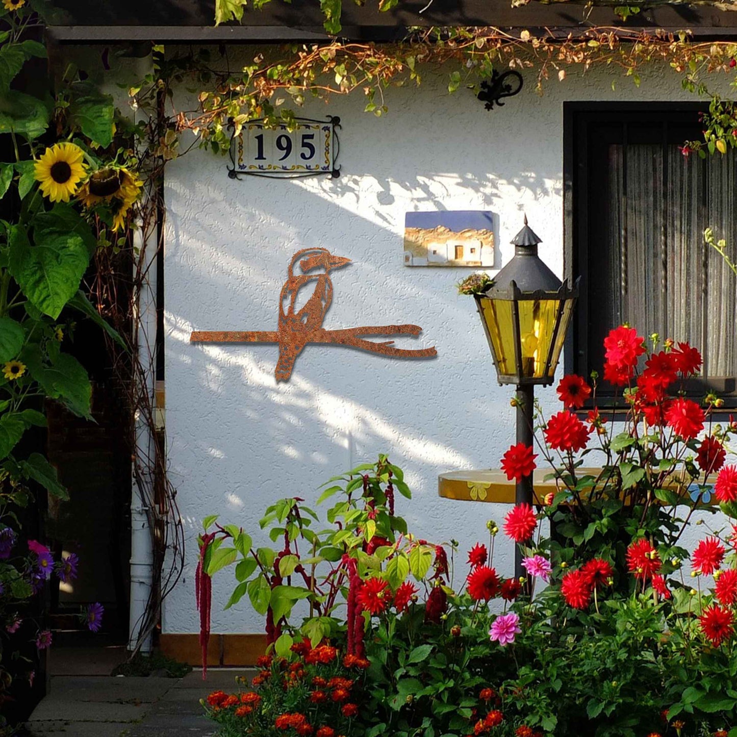 Metal garden decoration featuring a kingfisher perched on a branch with intricate cutout details and a rustic finish, designed to enhance walls or fences, adding a natural and elegant touch to outdoor spaces.