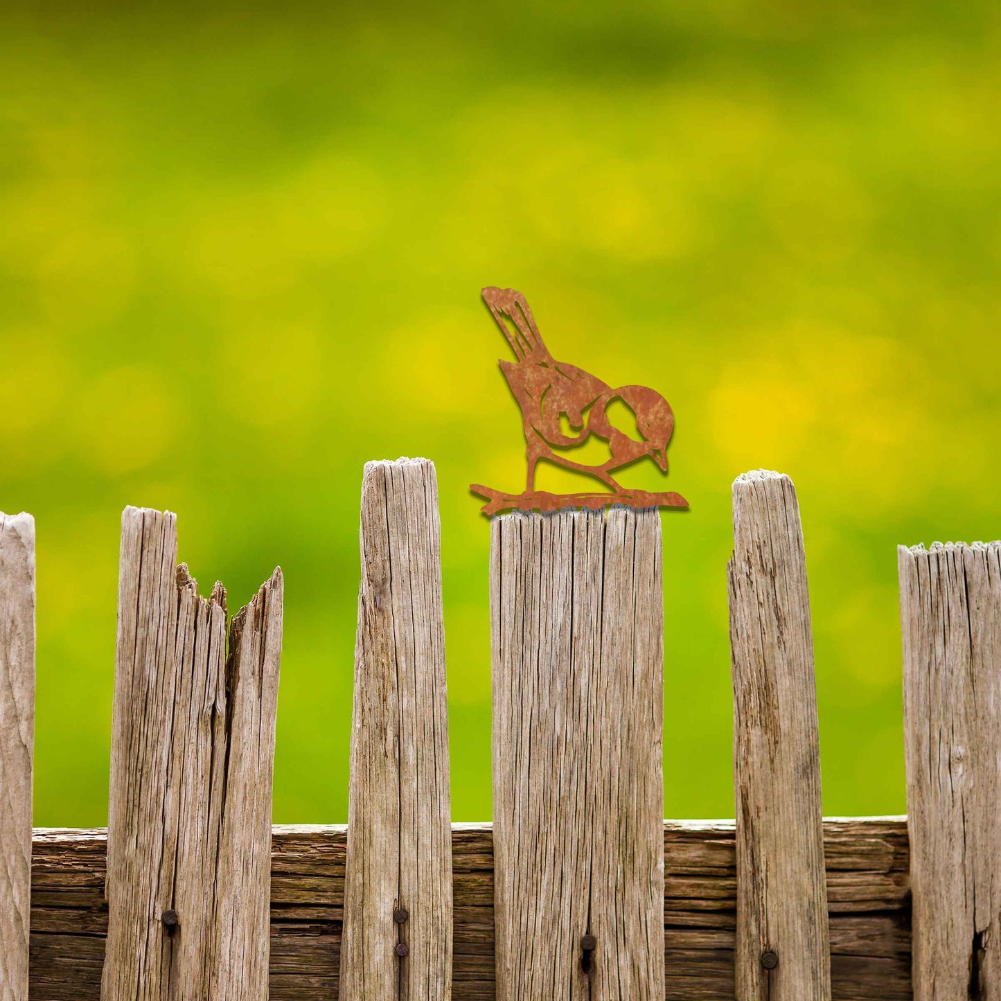 Metal garden decoration featuring a bird silhouette with a rustic finish, perched on a branch, designed to enhance fence tops or wooden posts, adding a natural and charming touch to outdoor spaces.