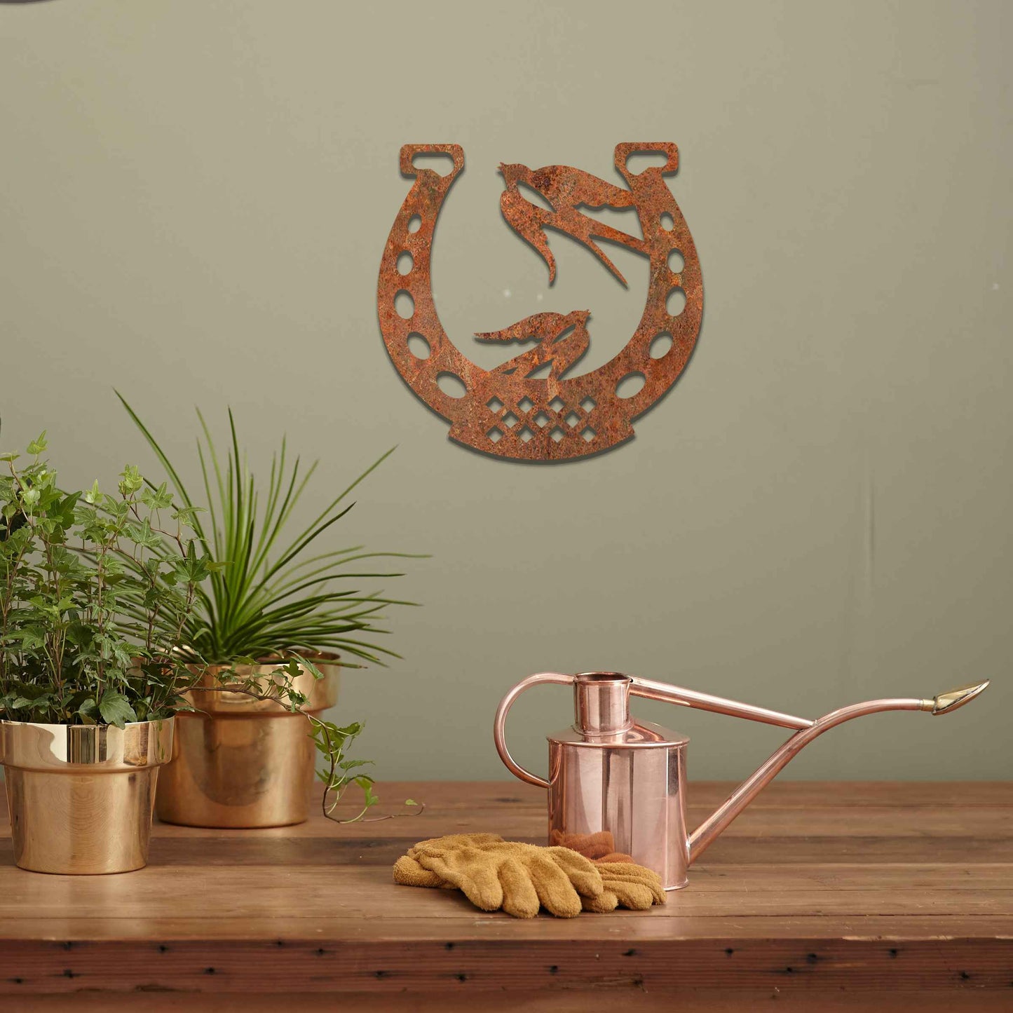 Metal garden decoration featuring two swallows perched within a horseshoe design, crafted with intricate detailing to symbolise luck and harmony, adding a rustic and charming touch to outdoor walls or fences.