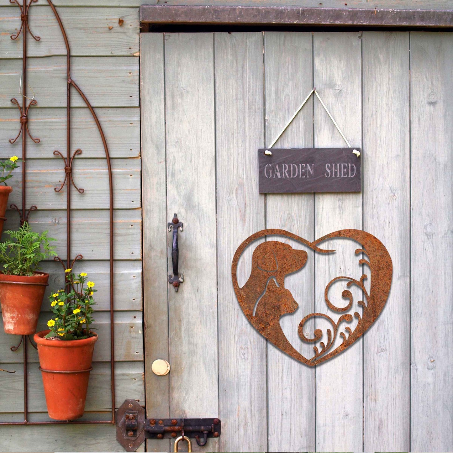 Metal garden decoration featuring a heart-shaped design with silhouettes of a dog and cat intertwined with elegant scrollwork, symbolising love for pets and adding a decorative charm to outdoor walls or garden spaces.
