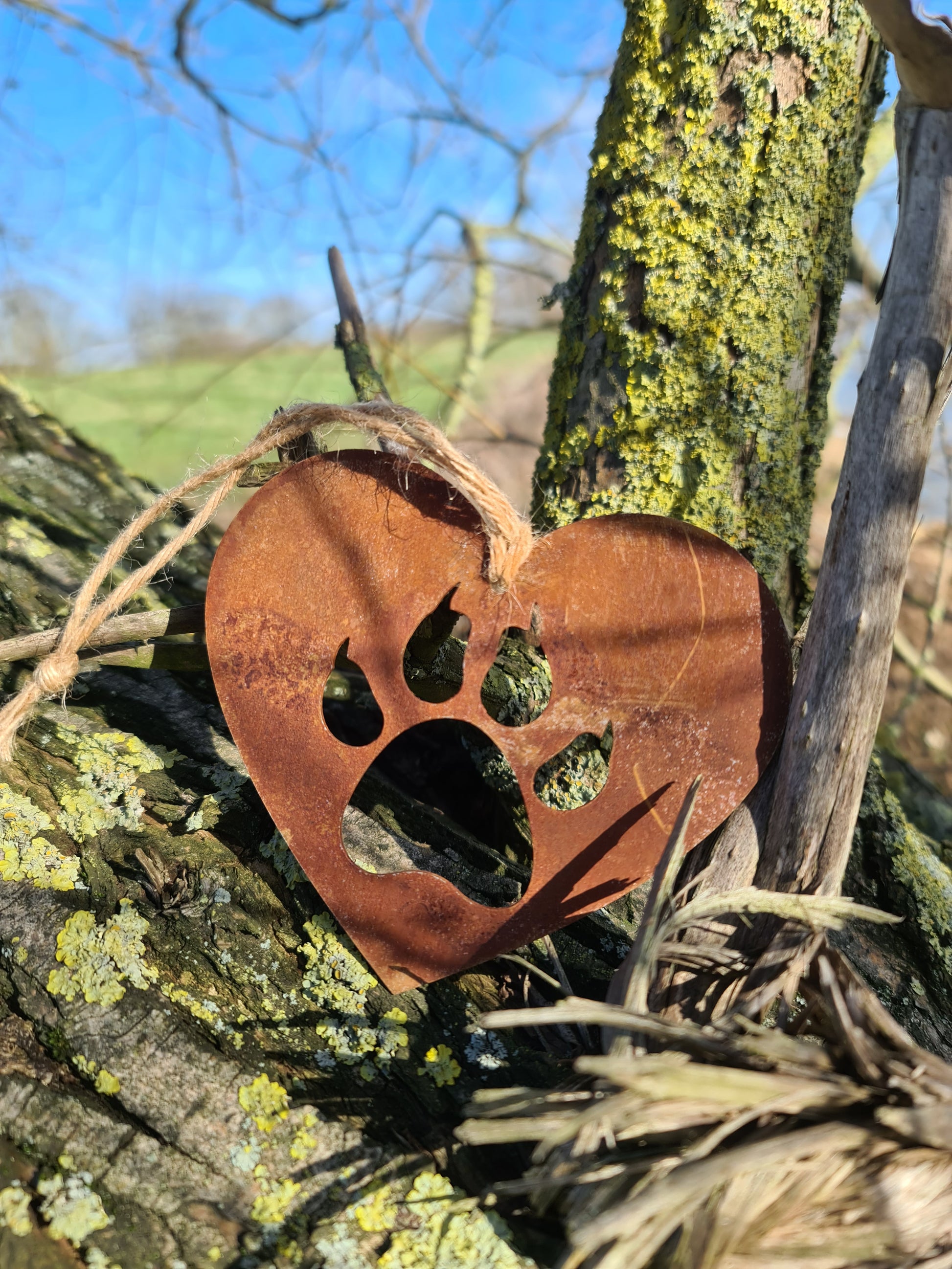 This heart-shaped metal ornament features a cat paw silhouette, symbolising love for feline companions. Its rustic finish adds a natural charm, and it includes a jute twine for easy hanging. Ideal for cat lovers and rustic-themed decor.