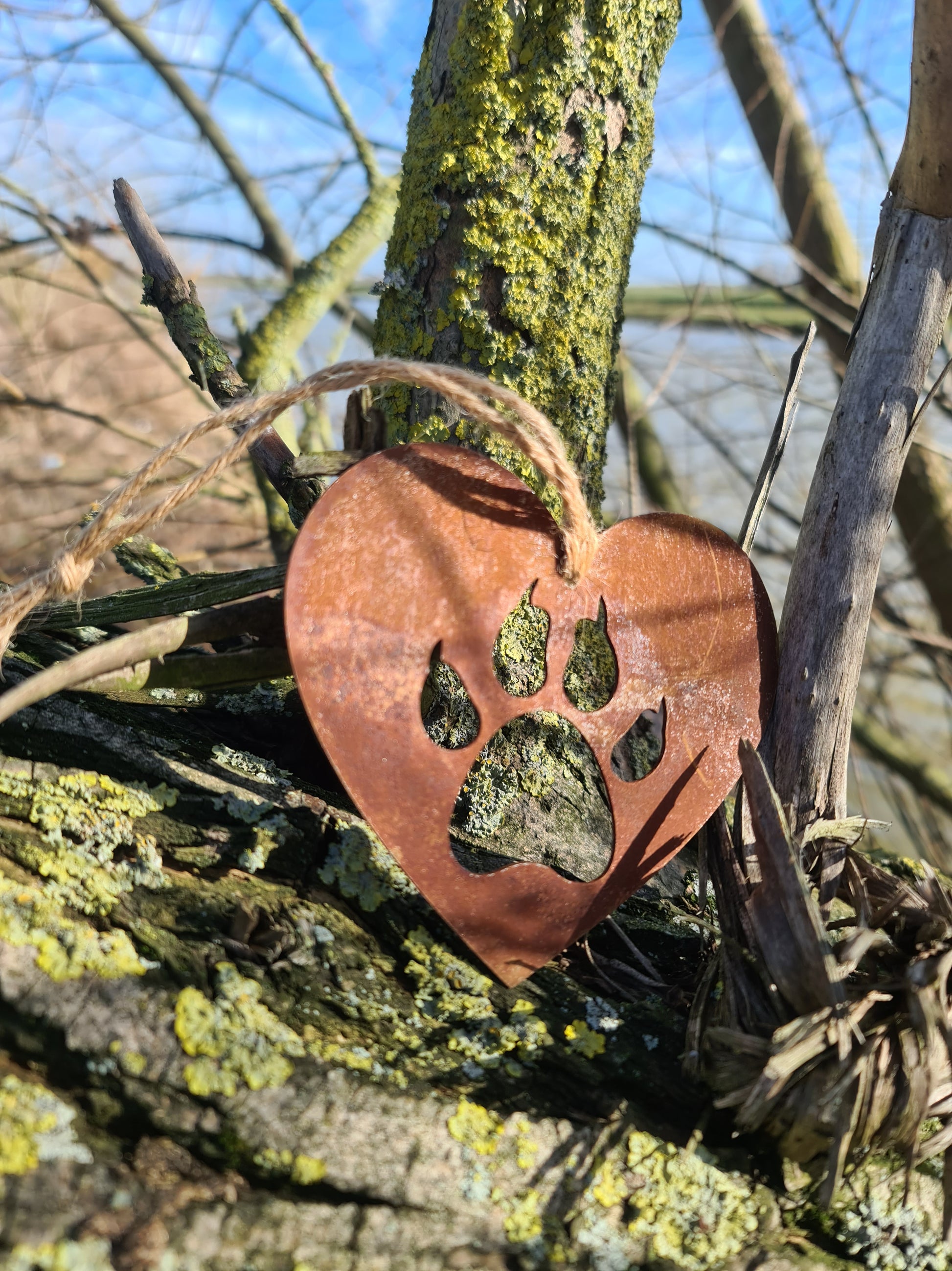 This heart-shaped metal ornament features a cat paw silhouette, symbolising love for feline companions. Its rustic finish adds a natural charm, and it includes a jute twine for easy hanging. Ideal for cat lovers and rustic-themed decor.