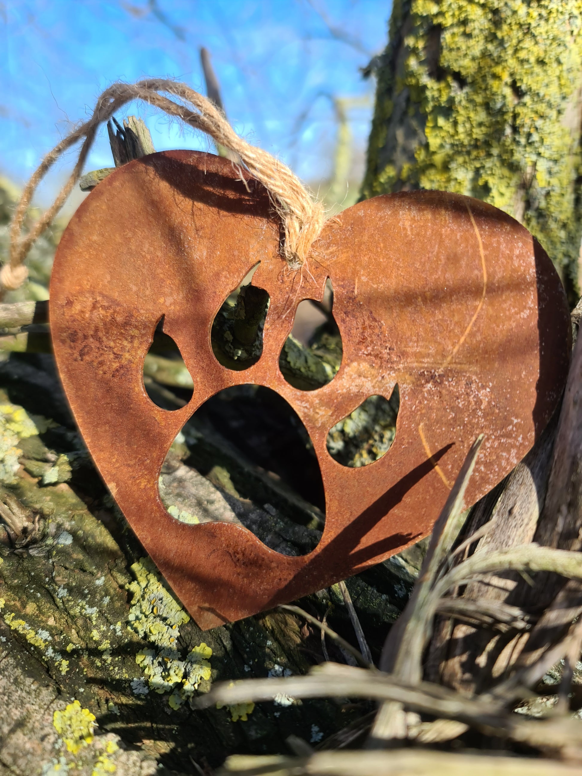This heart-shaped metal ornament features a cat paw silhouette, symbolising love for feline companions. Its rustic finish adds a natural charm, and it includes a jute twine for easy hanging. Ideal for cat lovers and rustic-themed decor.