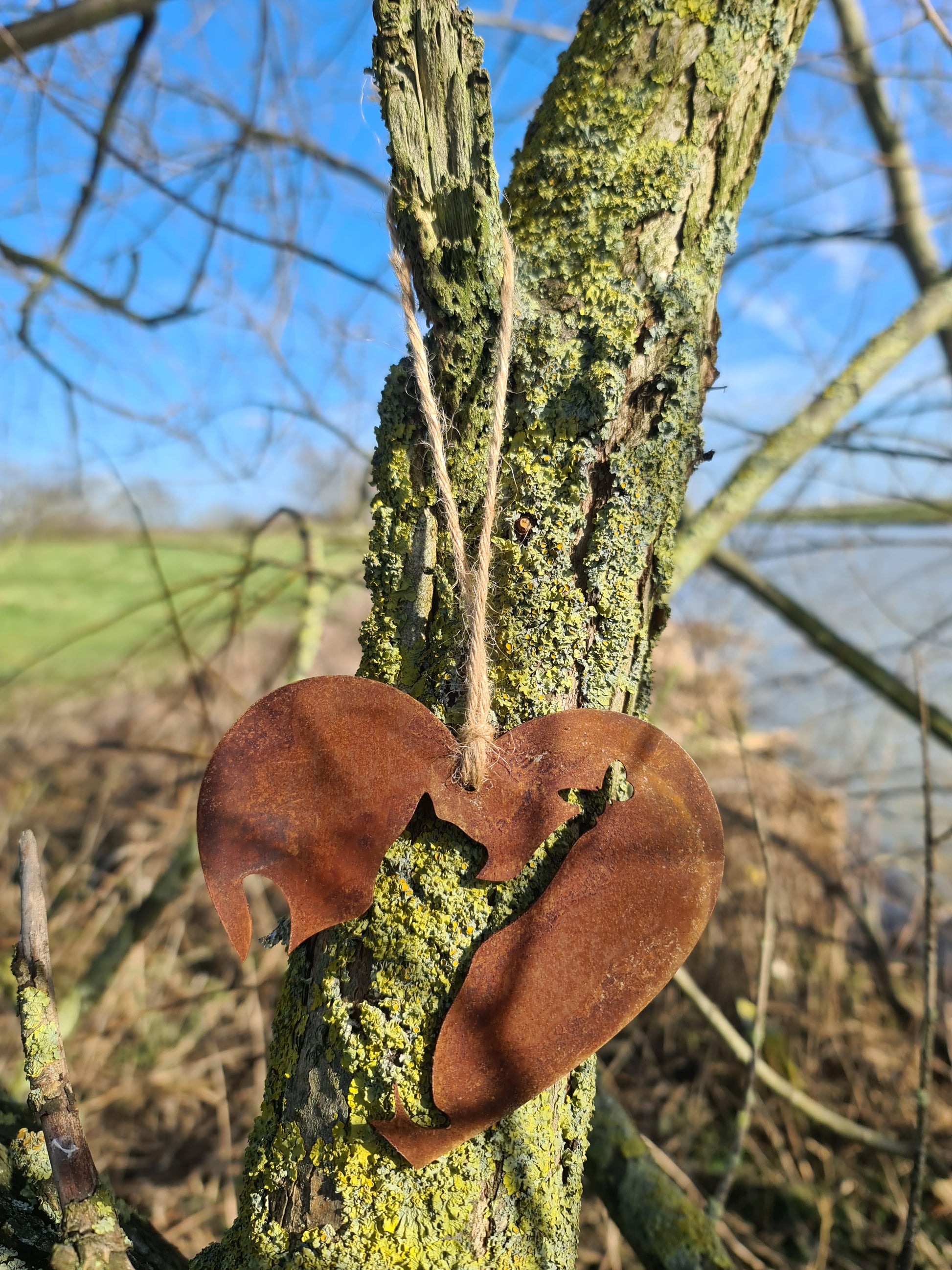 This heart-shaped metal ornament showcases a rustic cut-out silhouette of a cat, elegantly crafted for feline lovers. Its natural weathered finish and jute twine hanger make it a charming addition to any indoor or outdoor decor.