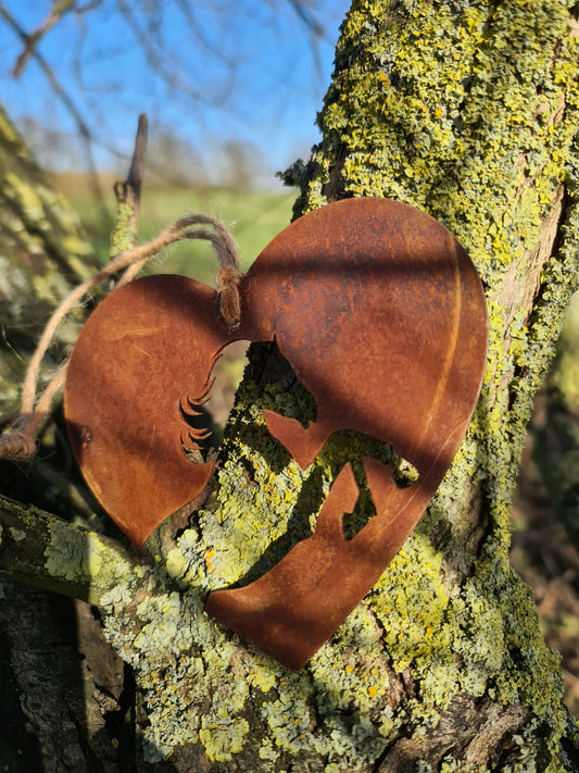 This heart-shaped metal ornament features a beautifully cut horse silhouette within the heart's frame. The rustic, weathered finish adds a natural and charming aesthetic. Complete with a jute twine for hanging, it's perfect for countryside or horse-themed decor.