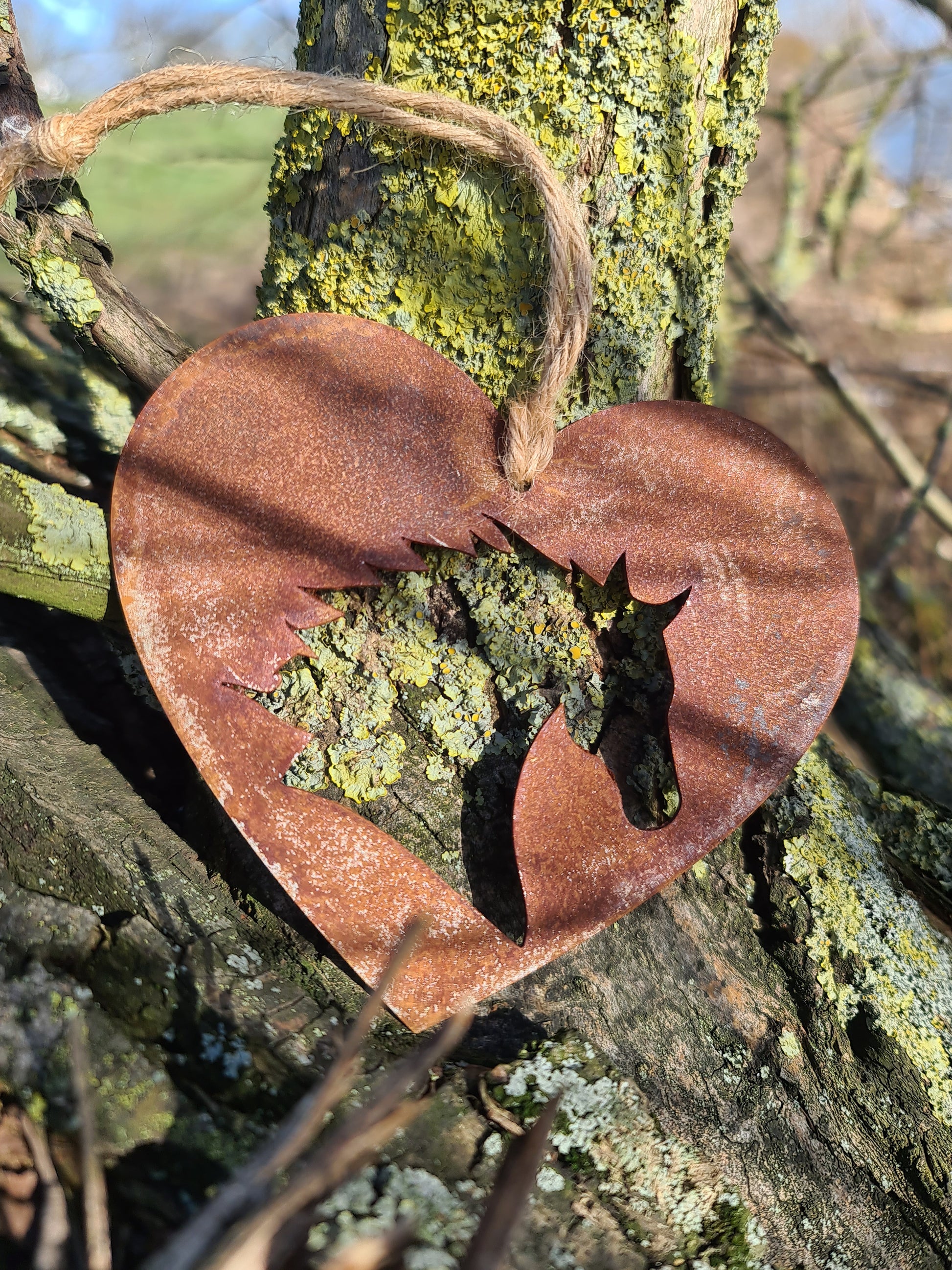 This rustic heart-shaped ornament features a detailed silhouette of a horse's head cut out in the center. The weathered, rusted finish adds a natural charm, while the jute twine provides a simple yet elegant way to hang it. Perfect for outdoor or rustic-themed decor.