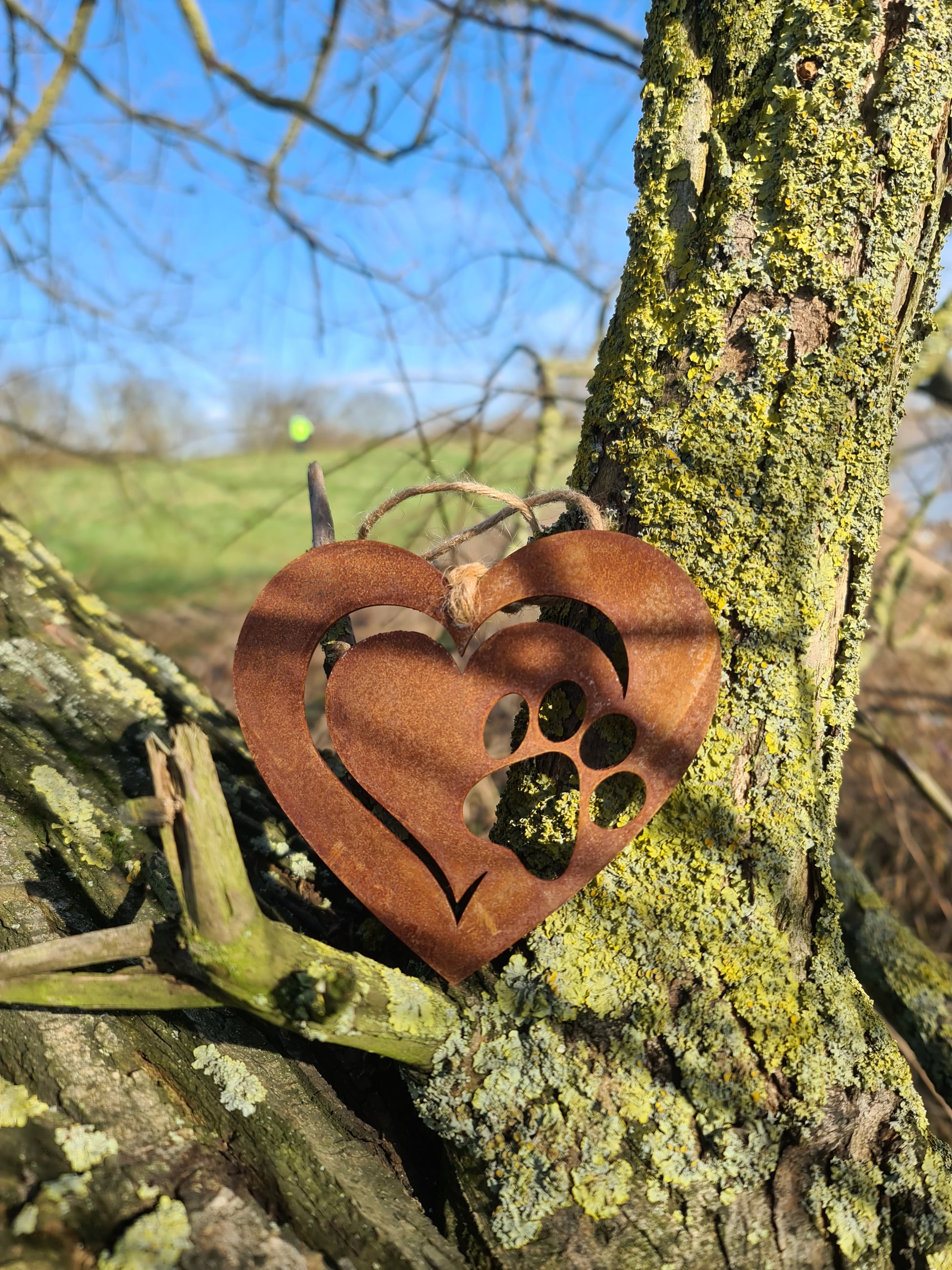 This is a heart-shaped metal ornament featuring a dog's paw print cut-out, beautifully crafted with a rustic finish. It is perfect for pet lovers and can be used as a decorative piece indoors or outdoors, adding a touch of charm and love for furry friends.