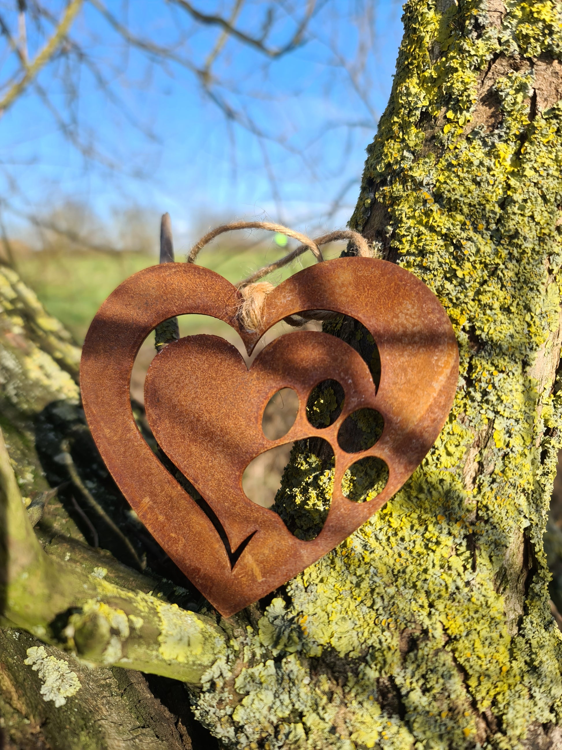 This is a heart-shaped metal ornament featuring a dog's paw print cut-out, beautifully crafted with a rustic finish. It is perfect for pet lovers and can be used as a decorative piece indoors or outdoors, adding a touch of charm and love for furry friends.