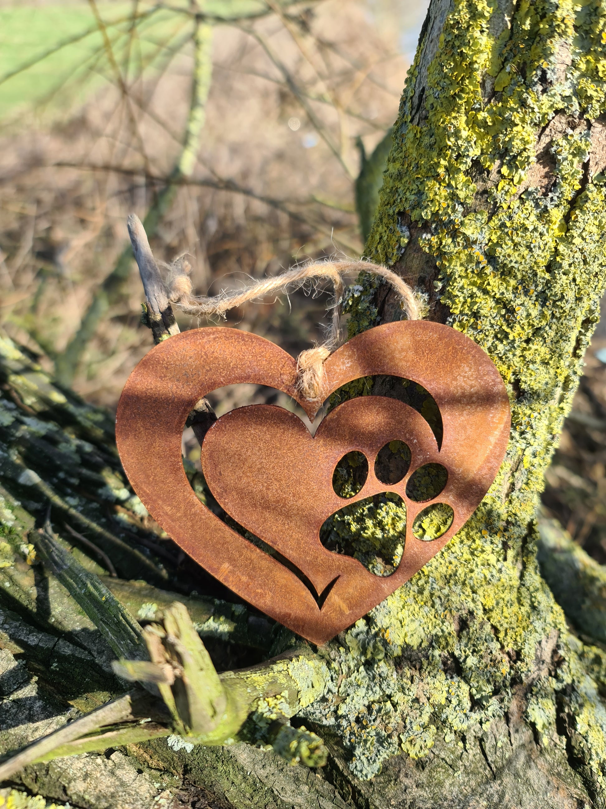 This is a heart-shaped metal ornament featuring a dog's paw print cut-out, beautifully crafted with a rustic finish. It is perfect for pet lovers and can be used as a decorative piece indoors or outdoors, adding a touch of charm and love for furry friends.