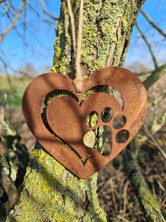 This is a heart-shaped metal ornament featuring a dog's paw print cut-out, beautifully crafted with a rustic finish. It is perfect for pet lovers and can be used as a decorative piece indoors or outdoors, adding a touch of charm and love for furry friends.