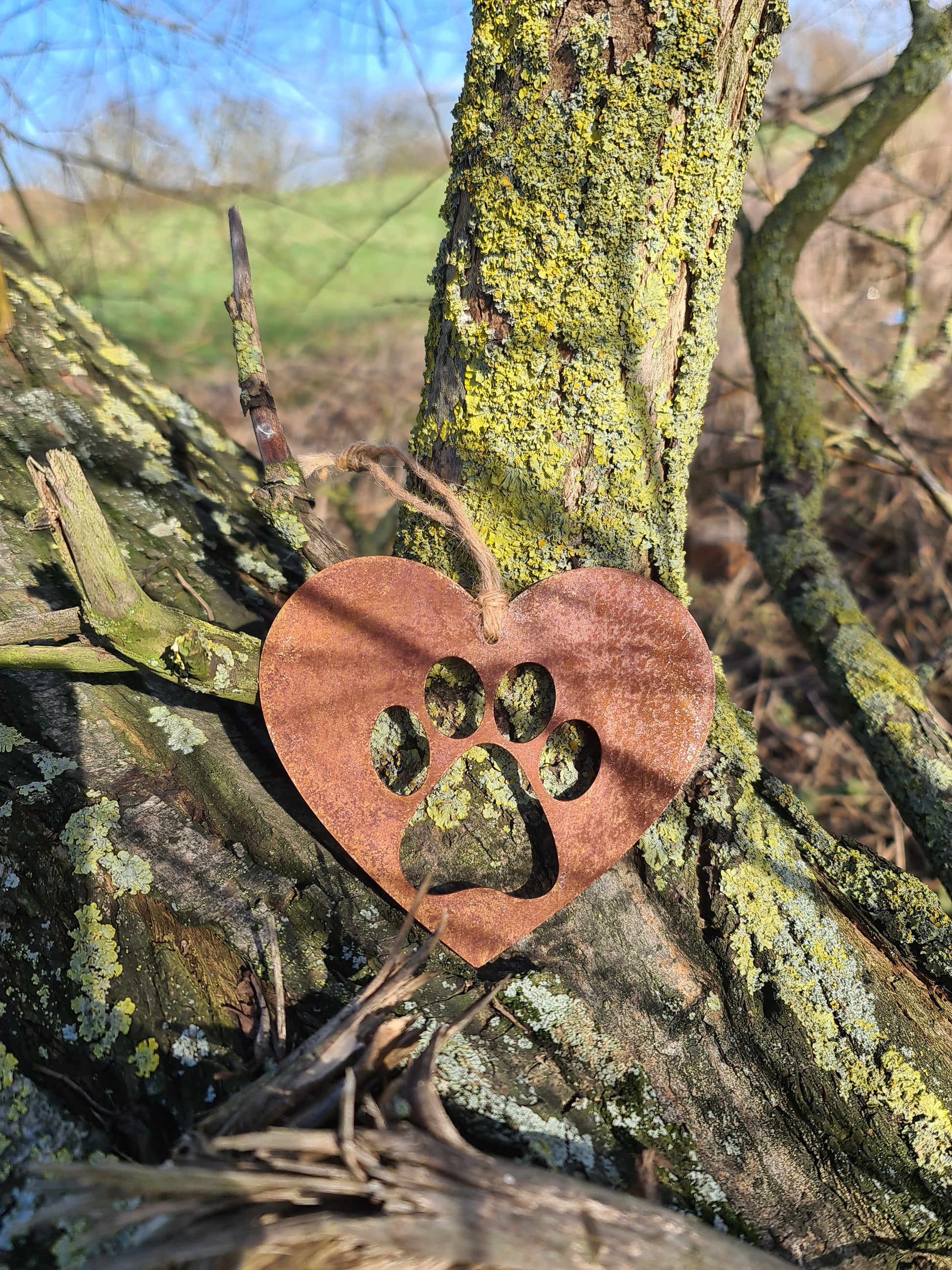 This is a heart-shaped metal decoration featuring a dog's paw print cut-out. Crafted with a rustic finish, this piece makes a thoughtful gift for dog lovers or a charming addition to any home or garden decor, celebrating the bond with a beloved pet.