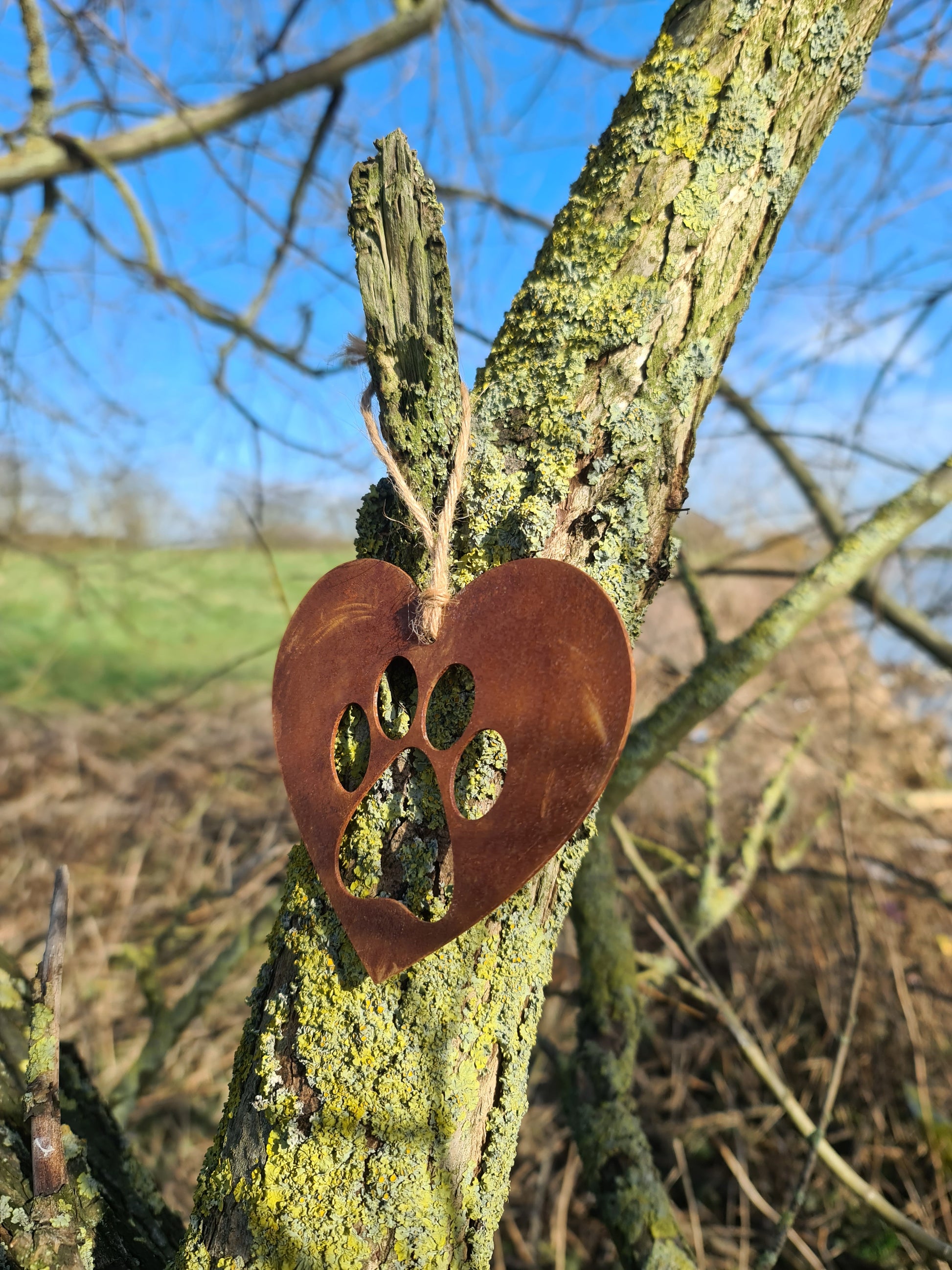 This is a heart-shaped metal decoration featuring a dog's paw print cut-out. Crafted with a rustic finish, this piece makes a thoughtful gift for dog lovers or a charming addition to any home or garden decor, celebrating the bond with a beloved pet.