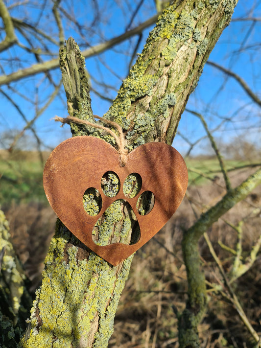 This is a heart-shaped metal decoration featuring a dog's paw print cut-out. Crafted with a rustic finish, this piece makes a thoughtful gift for dog lovers or a charming addition to any home or garden decor, celebrating the bond with a beloved pet.