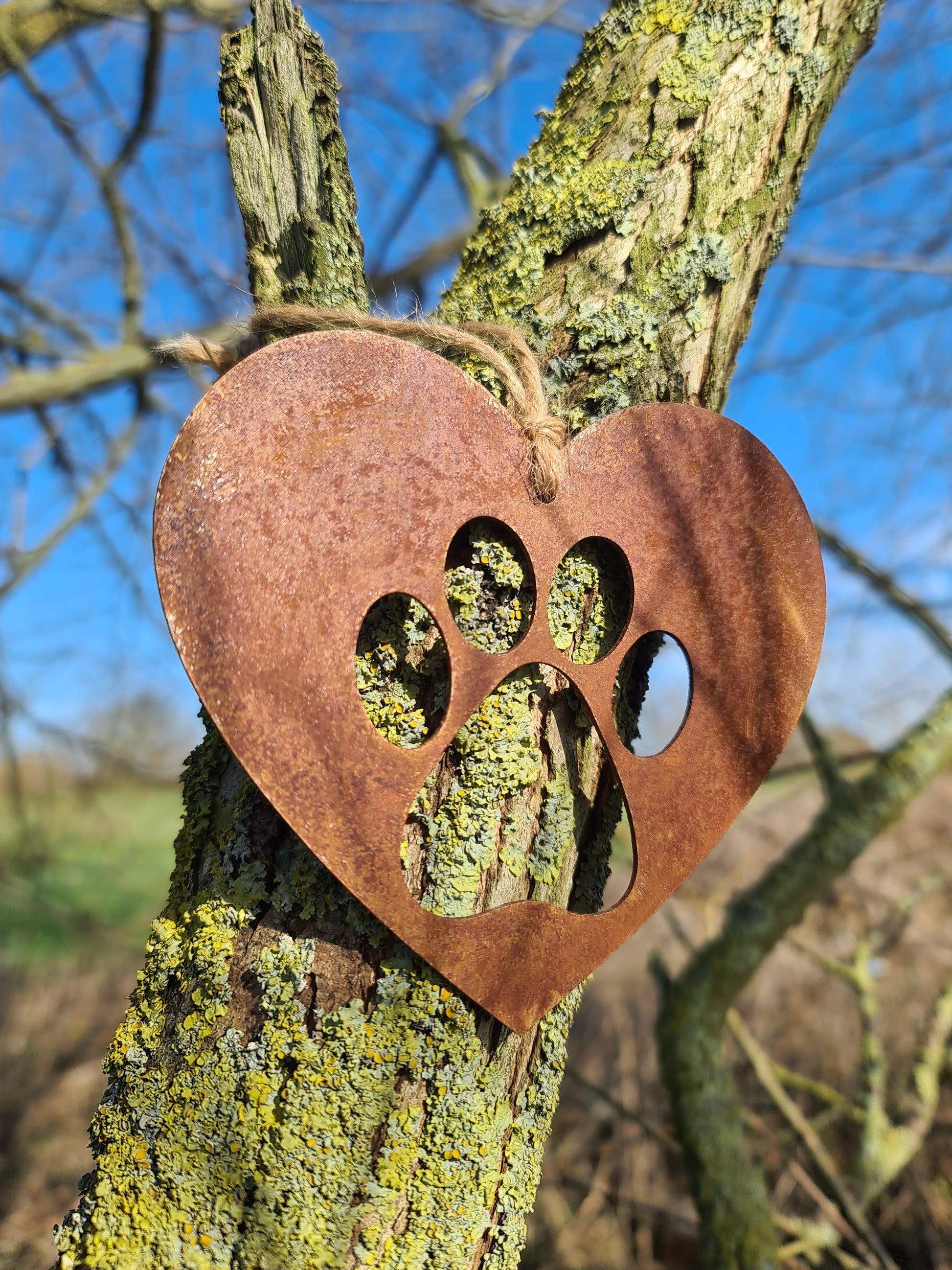 This is a heart-shaped metal decoration featuring a dog's paw print cut-out. Crafted with a rustic finish, this piece makes a thoughtful gift for dog lovers or a charming addition to any home or garden decor, celebrating the bond with a beloved pet.