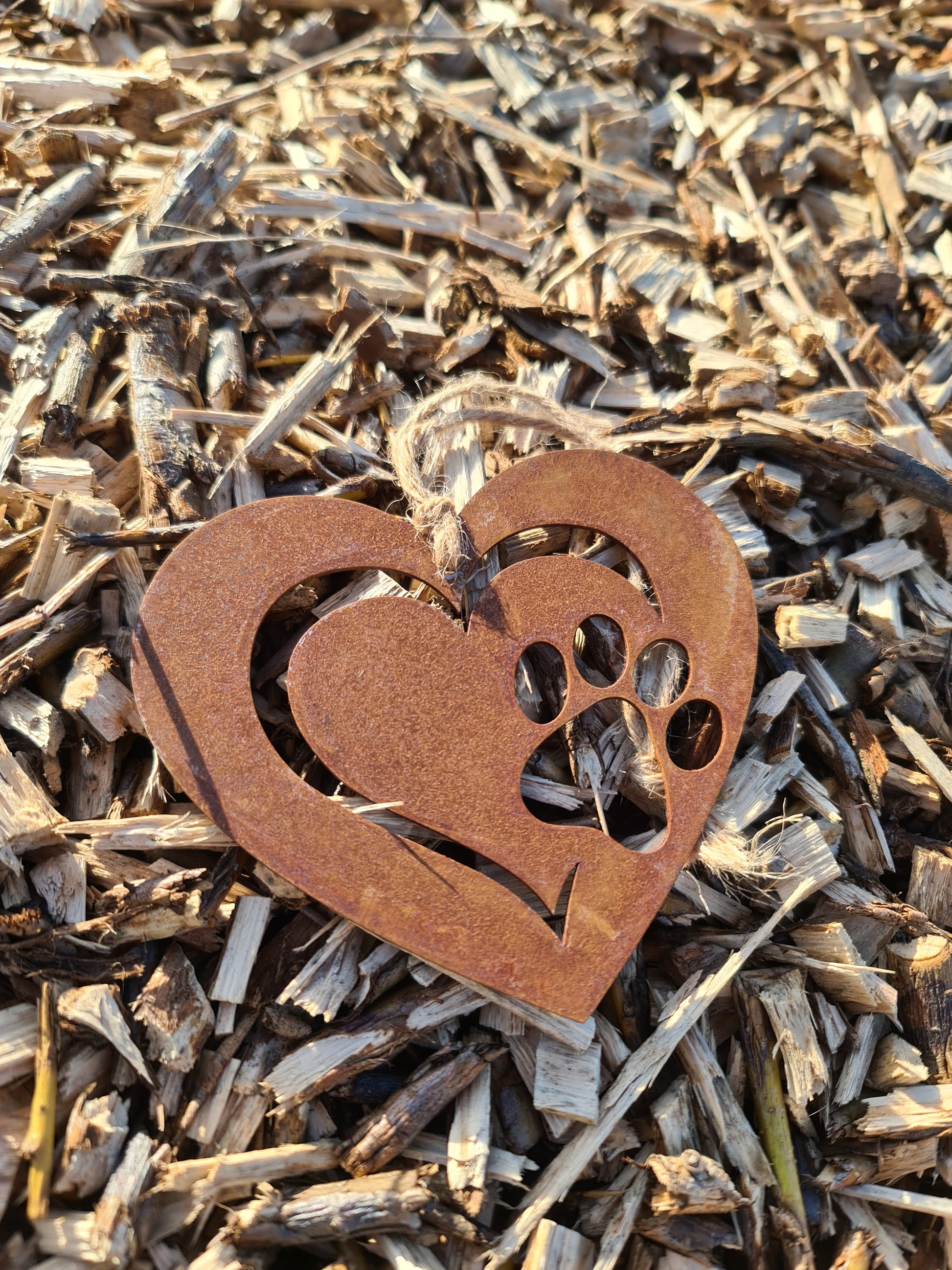 This is a heart-shaped metal ornament featuring a dog's paw print cut-out, beautifully crafted with a rustic finish. It is perfect for pet lovers and can be used as a decorative piece indoors or outdoors, adding a touch of charm and love for furry friends.