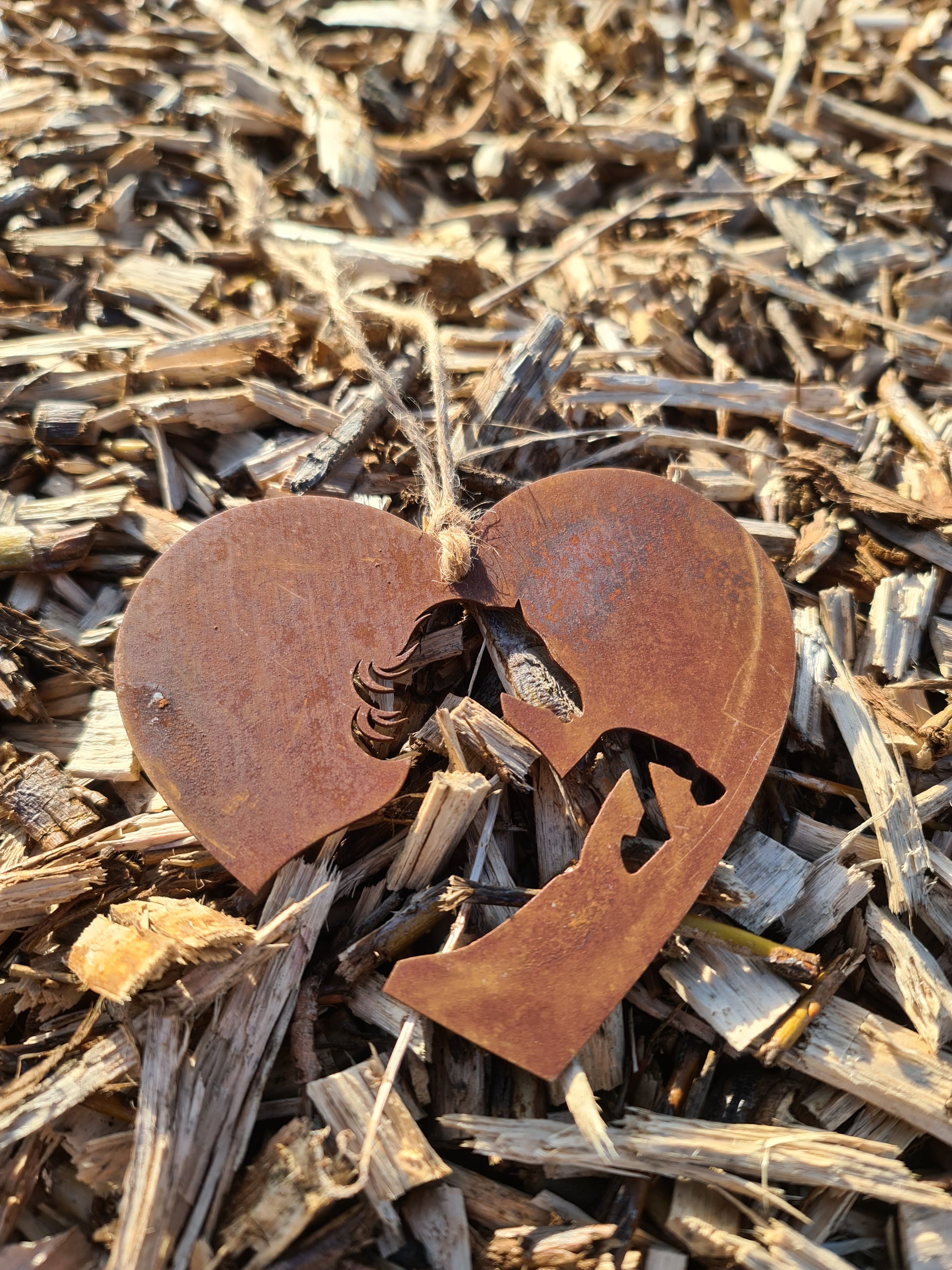 This heart-shaped metal ornament features a beautifully cut horse silhouette within the heart's frame. The rustic, weathered finish adds a natural and charming aesthetic. Complete with a jute twine for hanging, it's perfect for countryside or horse-themed decor.