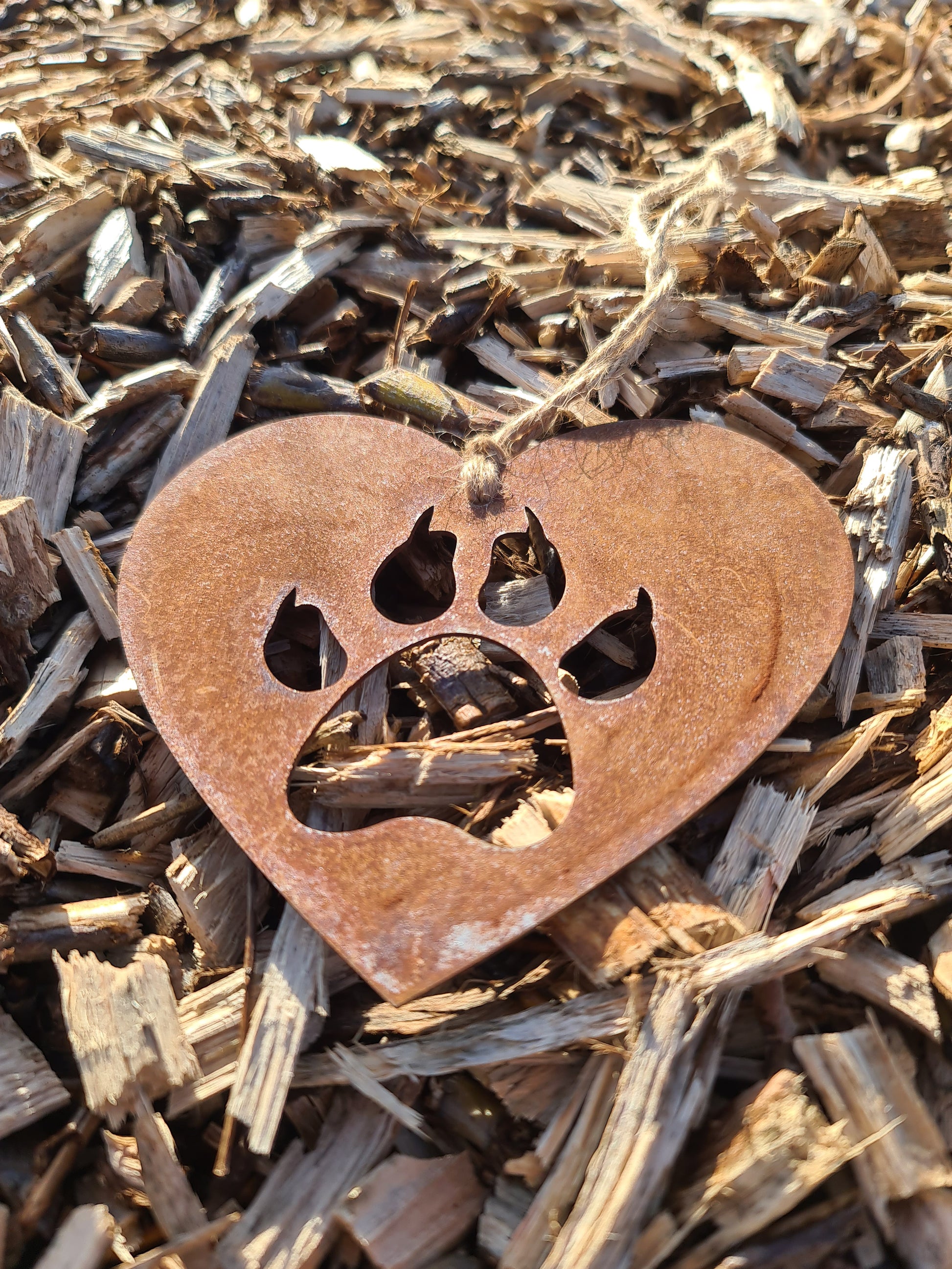 This heart-shaped metal ornament features a cat paw silhouette, symbolising love for feline companions. Its rustic finish adds a natural charm, and it includes a jute twine for easy hanging. Ideal for cat lovers and rustic-themed decor.