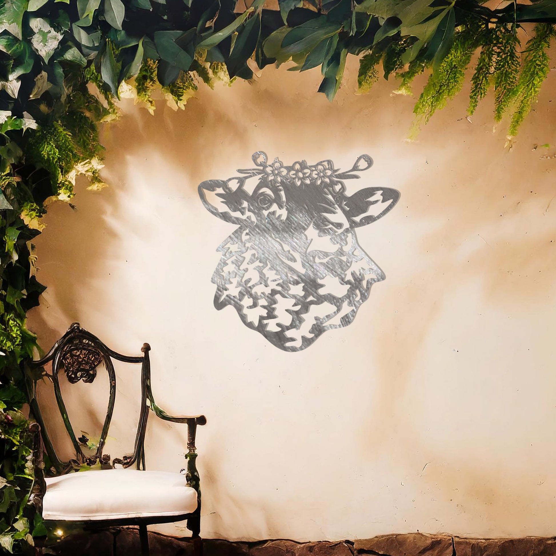 A metal wall art piece depicting a sheep adorned with a floral crown, exuding rustic charm and elegance. This intricate design brings a touch of countryside serenity to any modern or natural setting, complemented by its leafy surroundings.