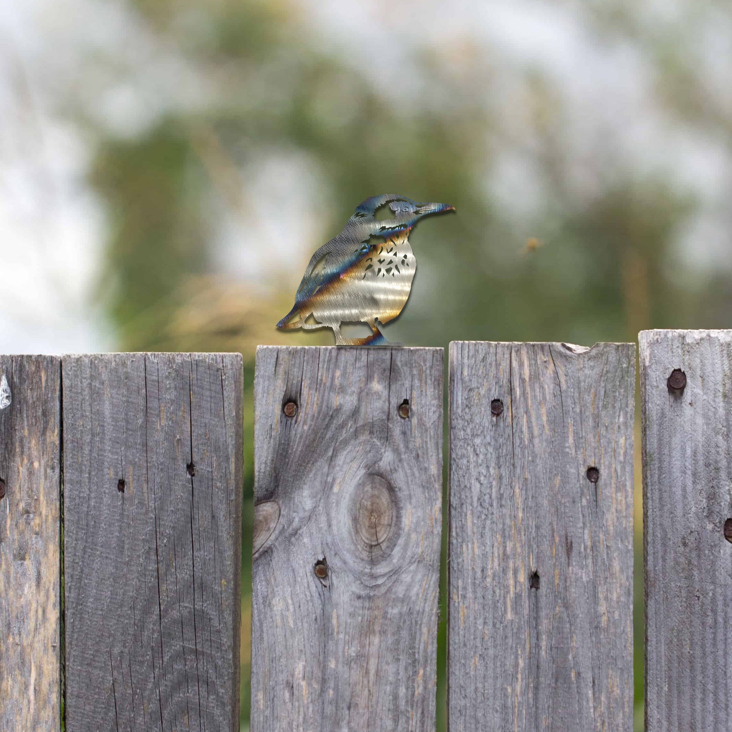 Metal wall art of a bird perched on a wooden fence post, featuring detailed wing and feather patterns. The bird is in a relaxed pose, surrounded by sunflowers, showcasing nature's beauty.