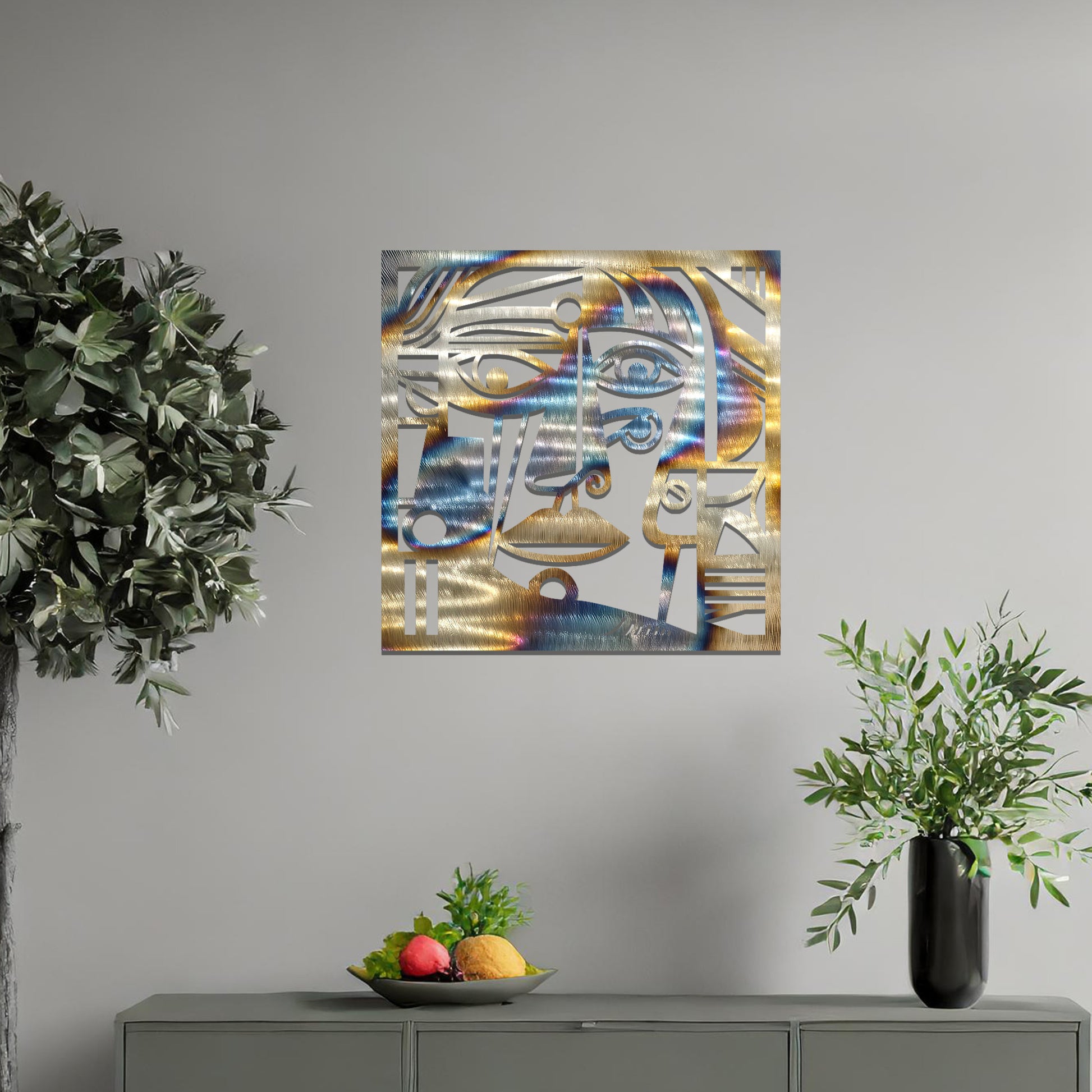 Geometric abstract face design cut from metal. The face features bold lines, sharp angles, and circular elements, creating a unique artistic representation. The art is displayed on a neutral wall in a modern room setting.