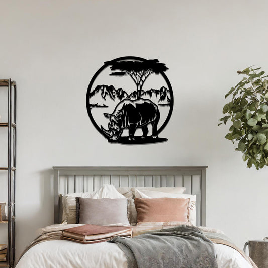 Metal wall art depicting a rhinoceros standing beneath a tree, with a mountain backdrop, framed in a circular design. The art is placed on a neutral wall within modern room decor, adding a natural and wild touch.