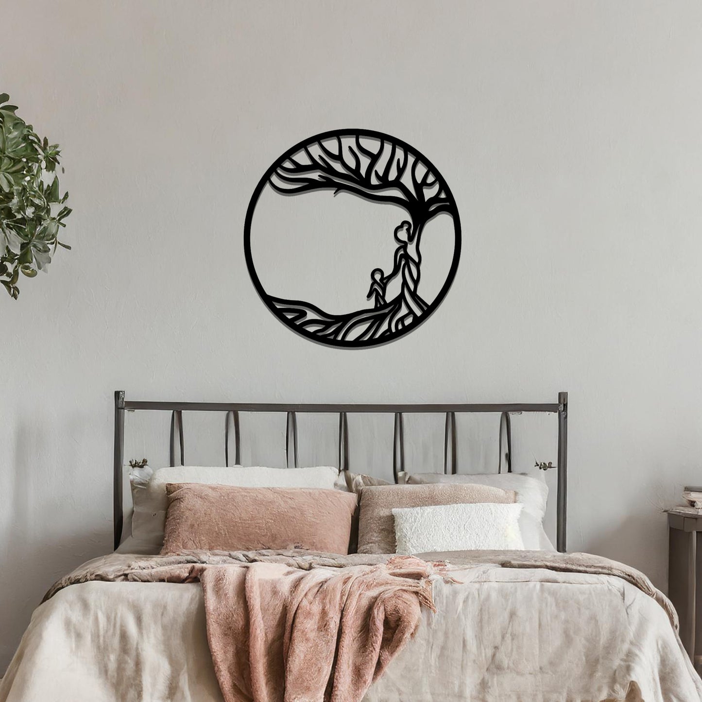 Metal wall art featuring a circular design with a symbolic tree and figures motif, depicting a parent and child under a tree with flowing branches, mounted on a neutral wall within modern room decor. The intricate design evokes warmth and connection, enhancing the aesthetic of the space.