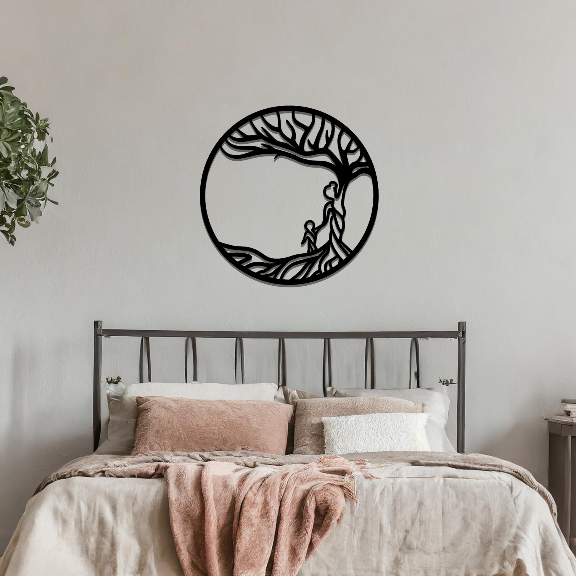 Metal wall art featuring a circular design with a symbolic tree and figures motif, depicting a parent and child under a tree with flowing branches, mounted on a neutral wall within modern room decor. The intricate design evokes warmth and connection, enhancing the aesthetic of the space.