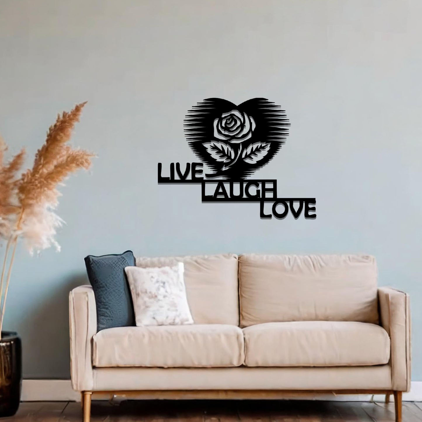 Metal wall art featuring the words "LIVE LAUGH LOVE" alongside a rose within a heart shape, with bold lines and intricate design. The art is displayed on a neutral wall within modern room decor, offering a stylish and motivational accent to the space.
