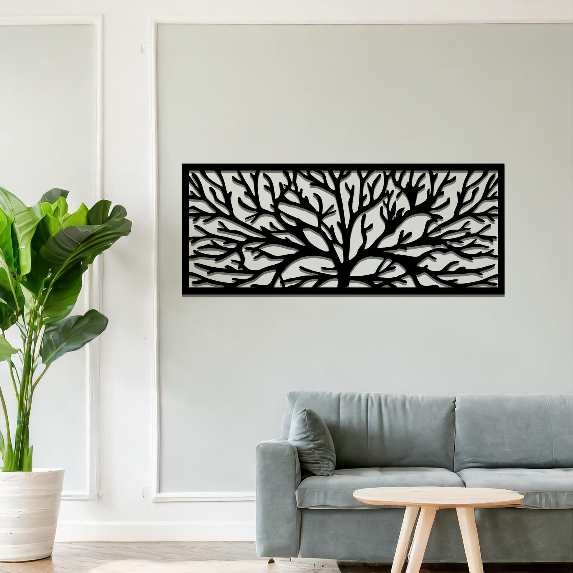 A metal wall art design featuring a detailed tree silhouette with sprawling branches, enclosed in a rectangular frame. The art is displayed on a neutral wall in a modern living room, complementing the contemporary decor and natural elements in the space.
