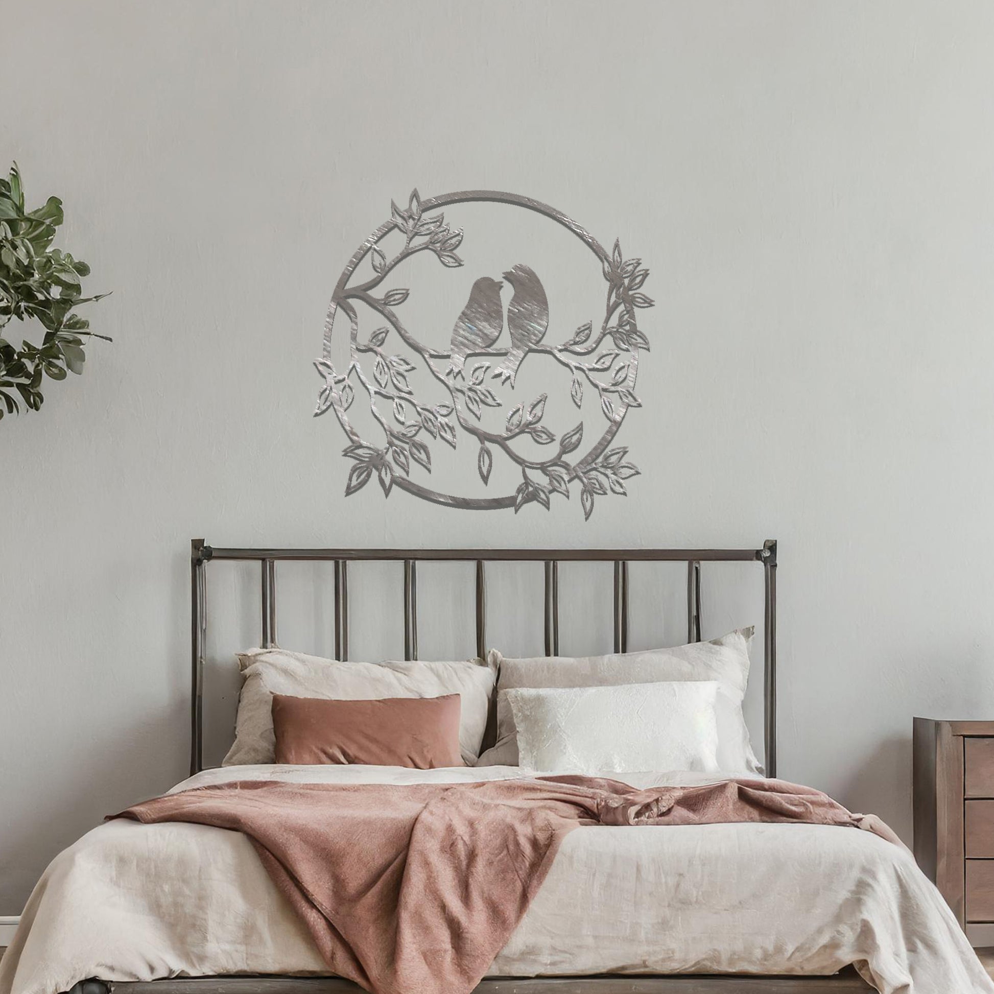 Metal wall art featuring a circular design with two birds perched on a branch surrounded by intricate leaves, adding a charming focal point to a beautifully styled living space.