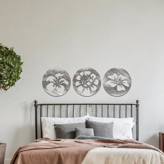 A set of three circular metal panels featuring floral designs, each panel showcasing a different flower in intricate detail. The artwork is displayed on a neutral wall, enhancing the serene and natural ambiance of the bedroom.